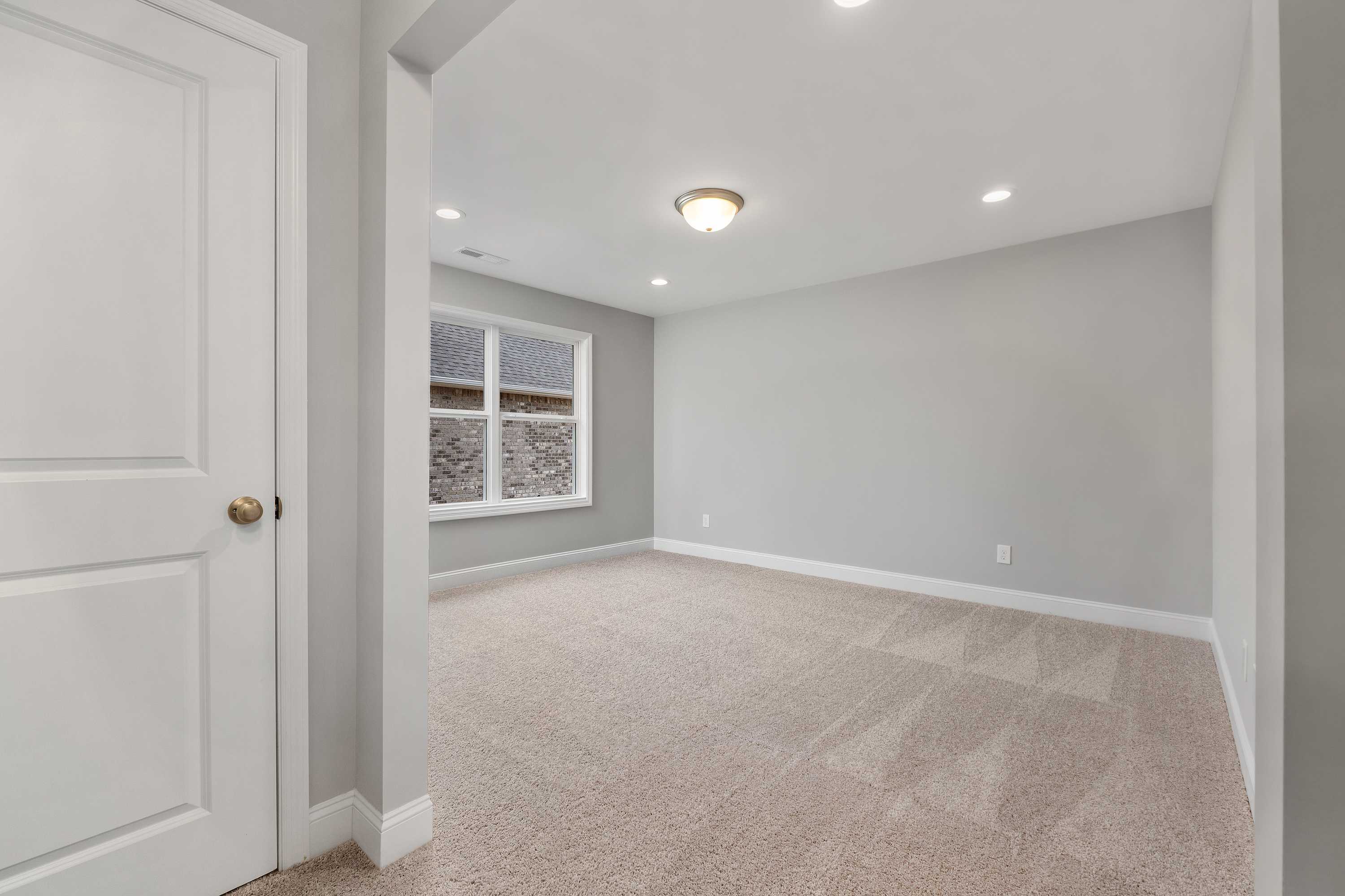 Spacious empty master bedroom in The Aiken home design with gray walls, beige carpet, large window, and white trim