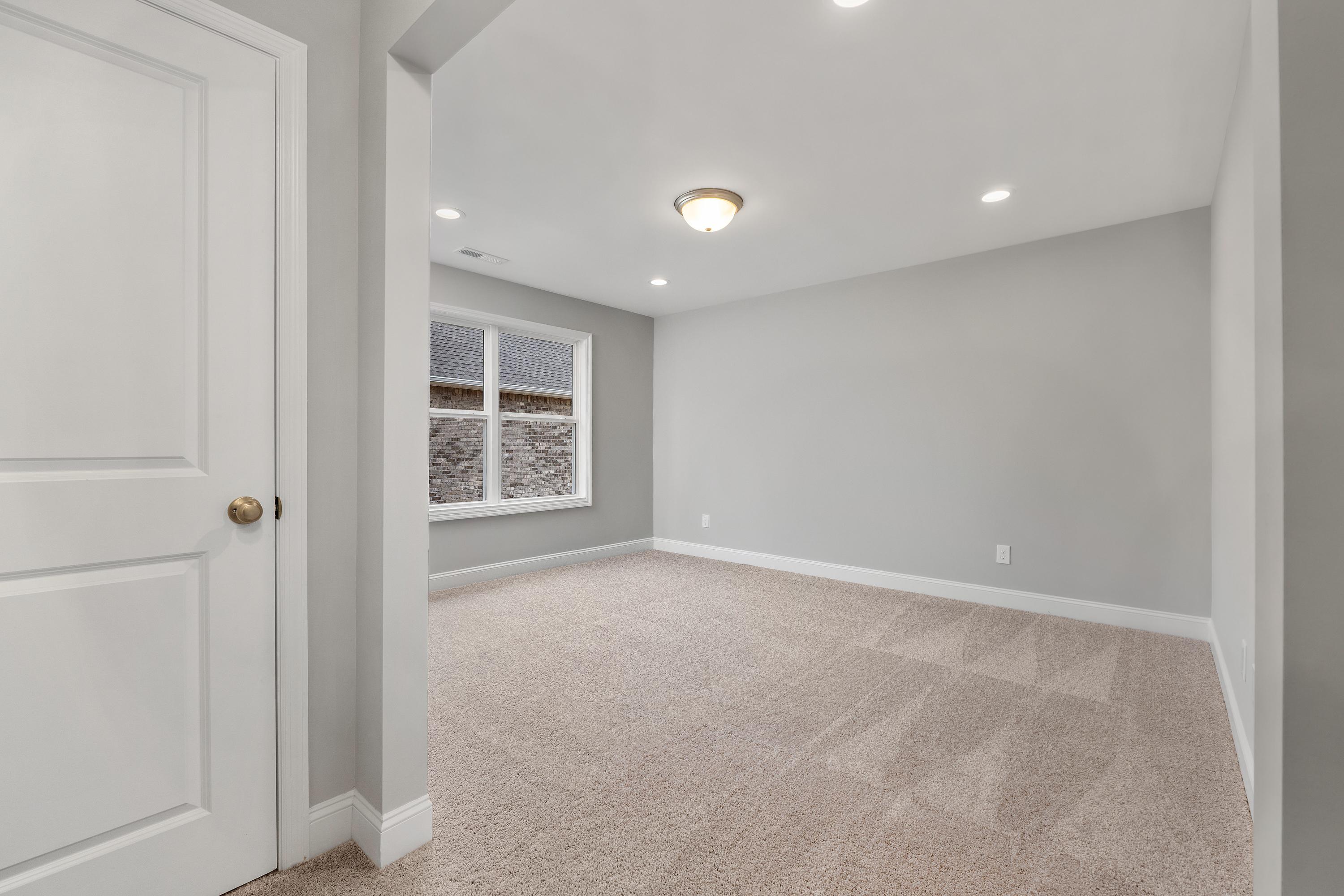 Spacious empty master bedroom in The Aiken home design with gray walls, beige carpet, large window, and white trim