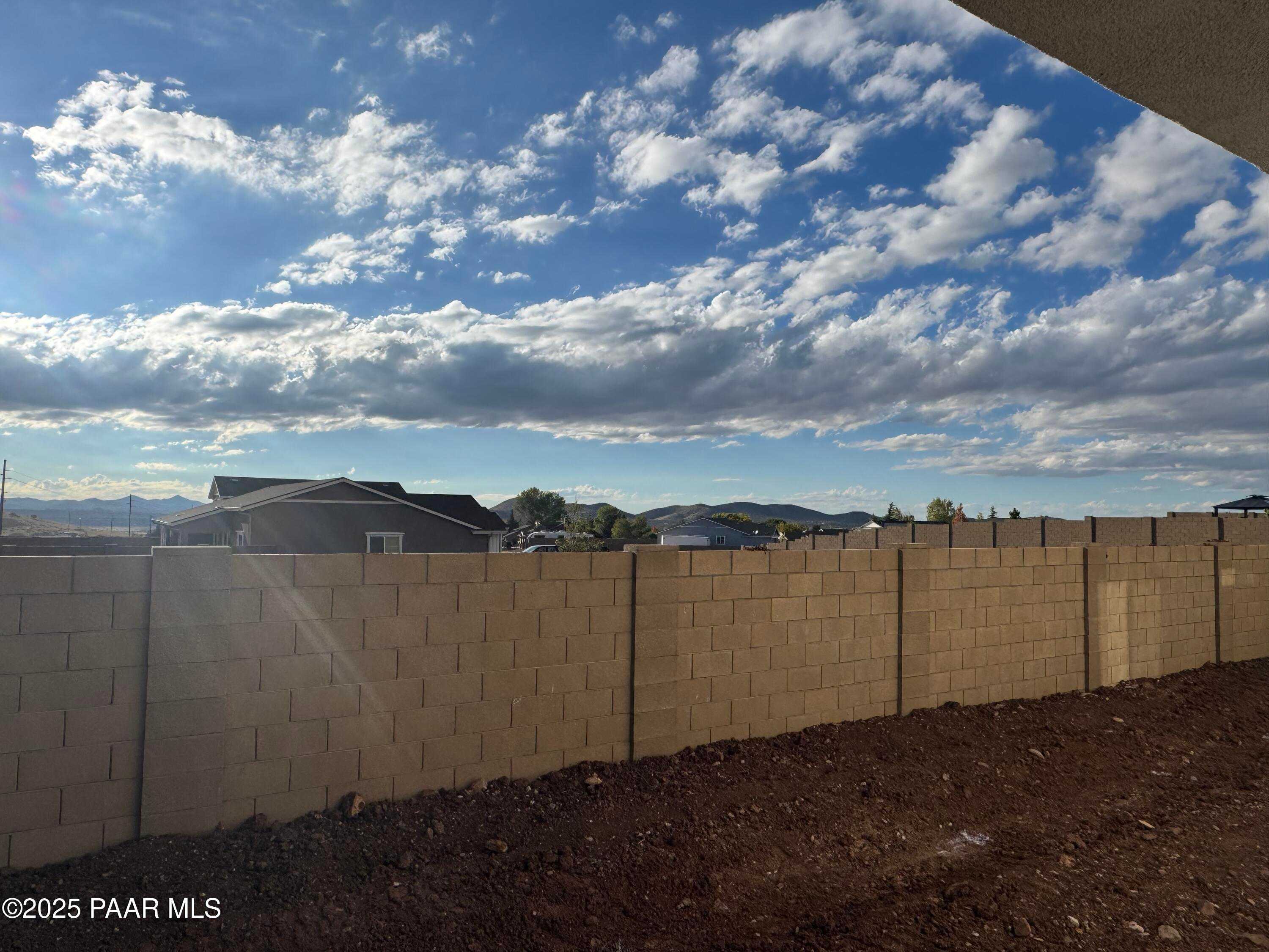 Spacious backyard with beige block fence, mountain views, and sunny skies in 3-bedroom Evermore Homes Sunrise A, Prescott Valley, AZ
