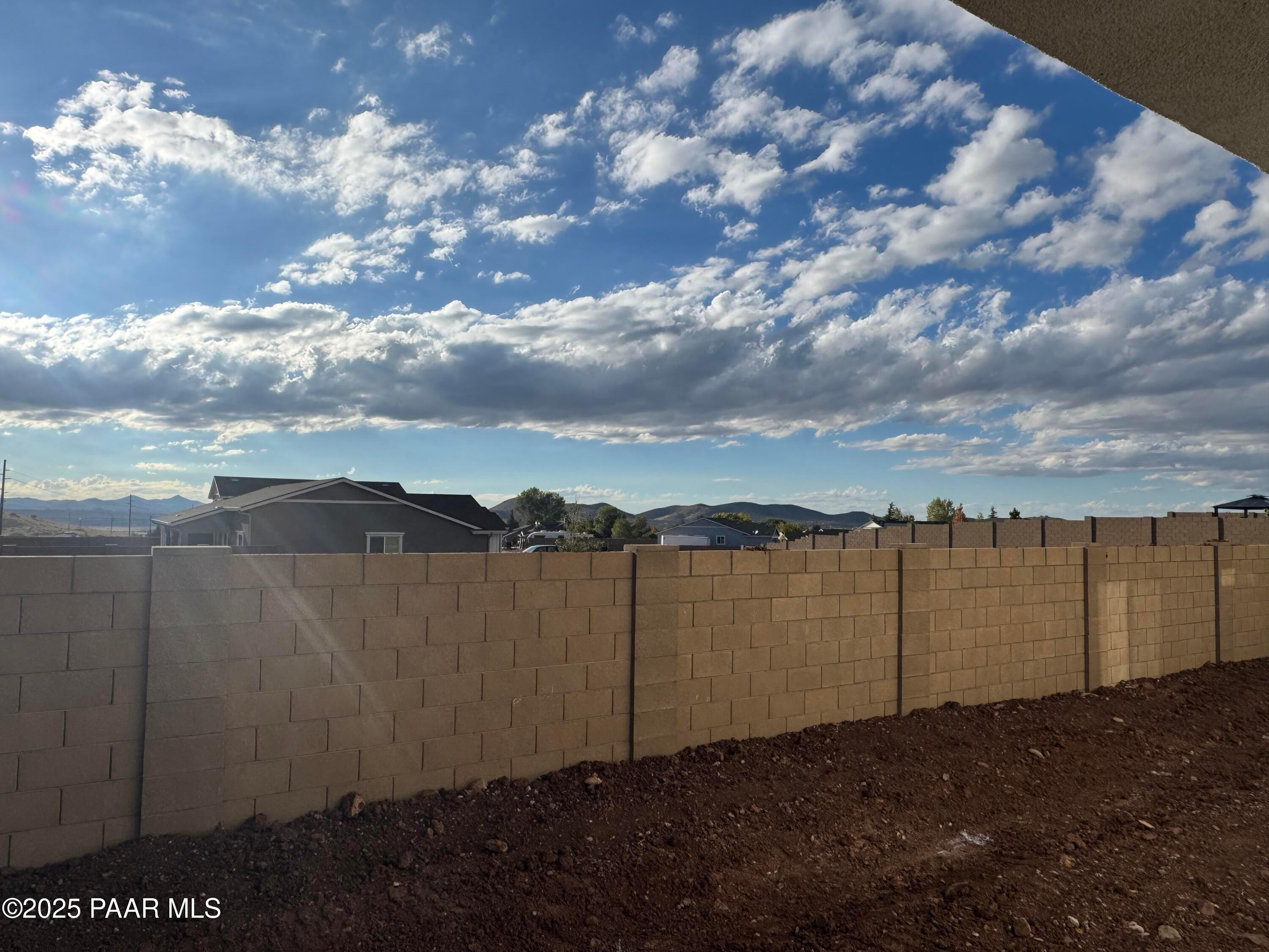 Spacious backyard with beige block fence, mountain views, and sunny skies in 3-bedroom Evermore Homes Sunrise A, Prescott Valley, AZ