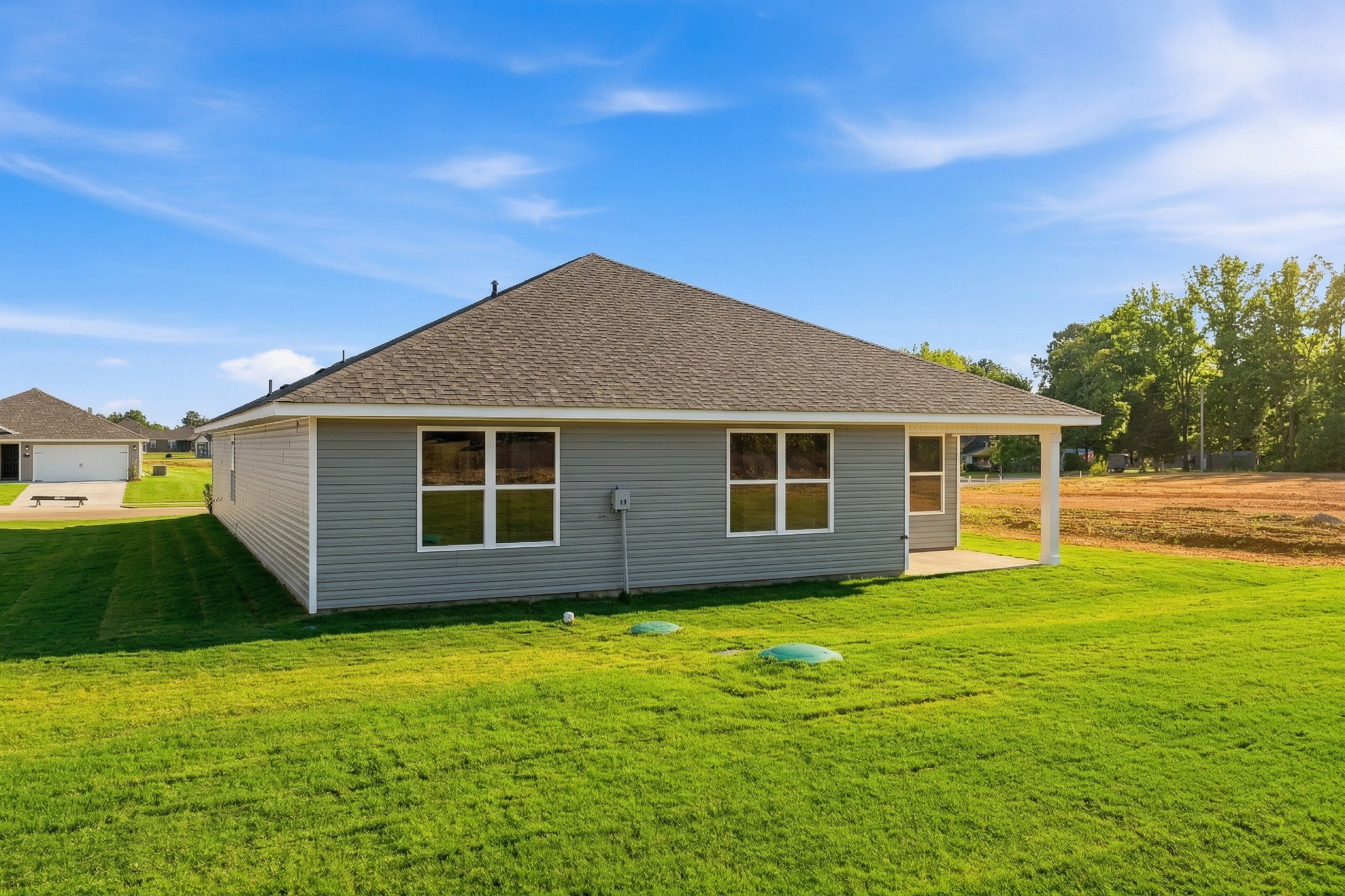 Side view of The Daphne V single-story home with gray siding, shingled roof, covered porch, and green lawn in Meridianville Alabama