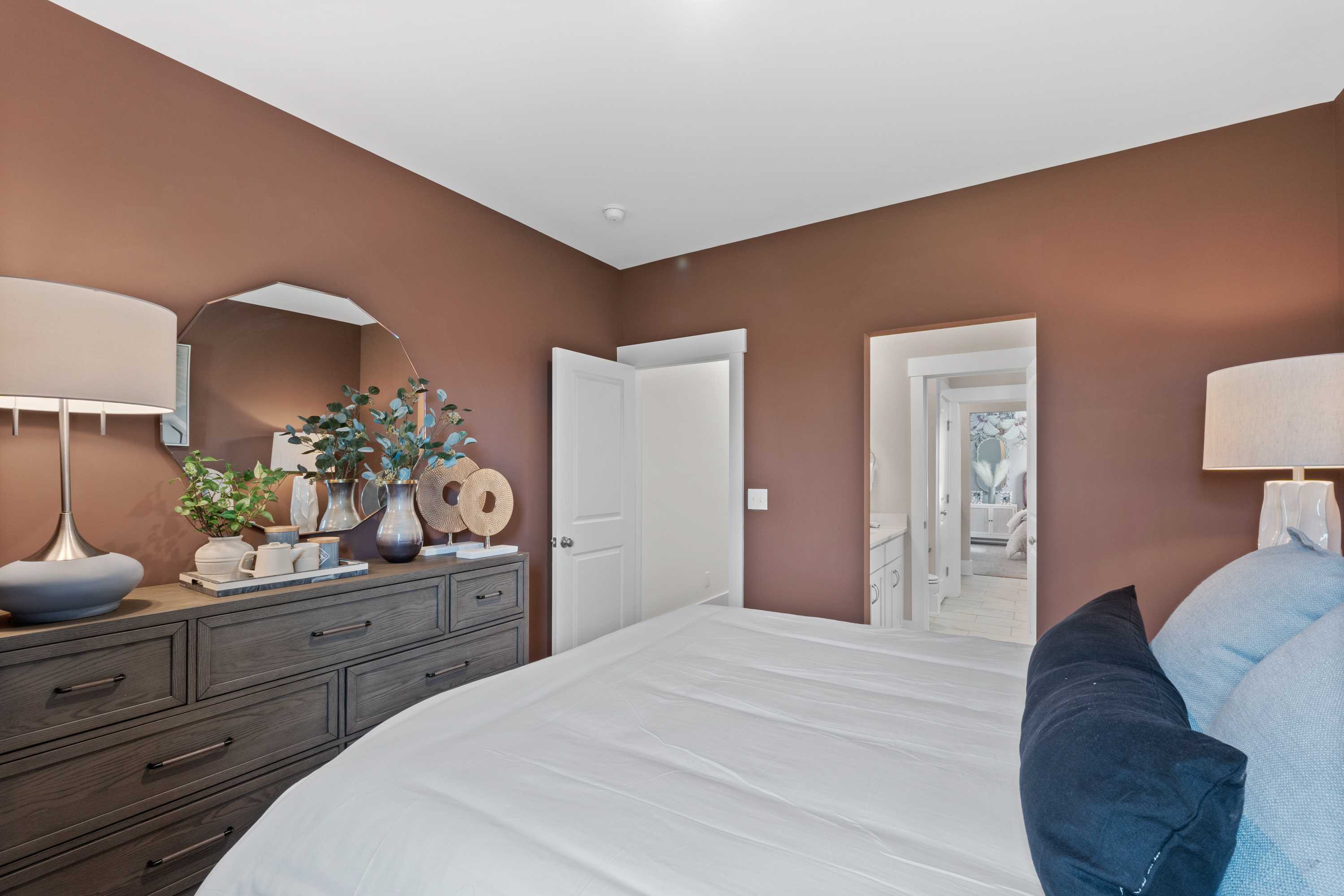 Cozy primary bedroom at Creekside in Harvest Alabama by Davidson Homes with king bed wooden dresser modern lamps and plants