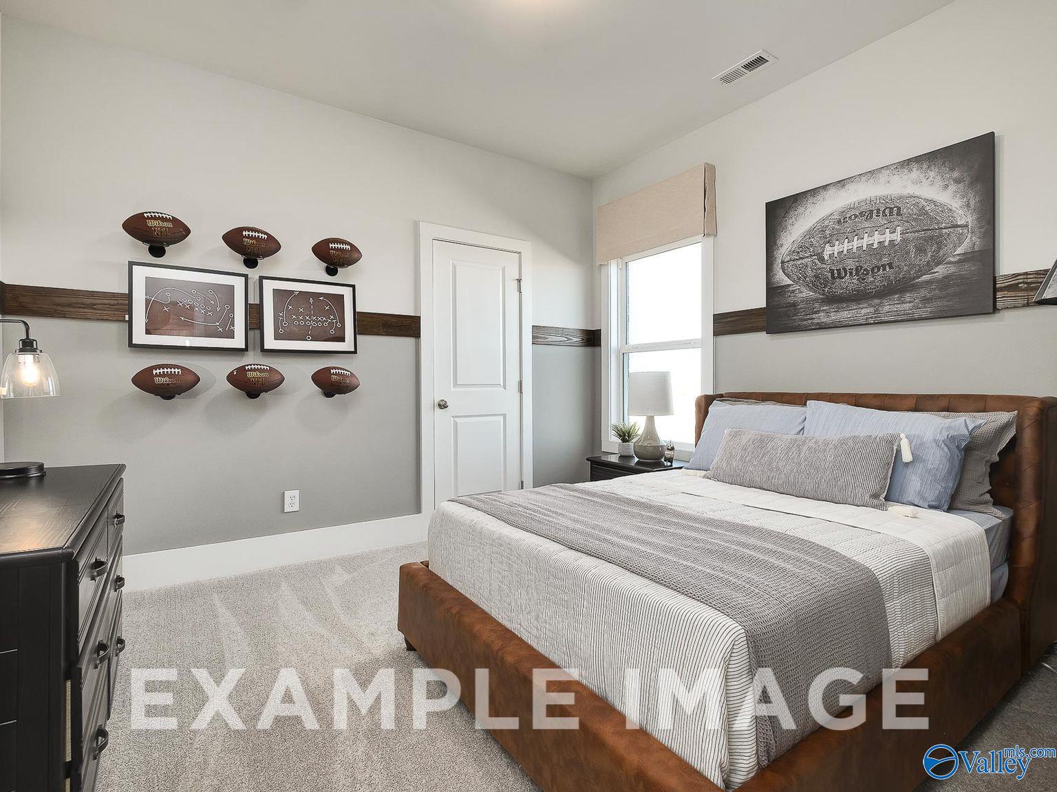 Football-themed bedroom with mounted helmets, framed artwork, and queen bed in Davidson Homes The Everett B, Toney, Alabama