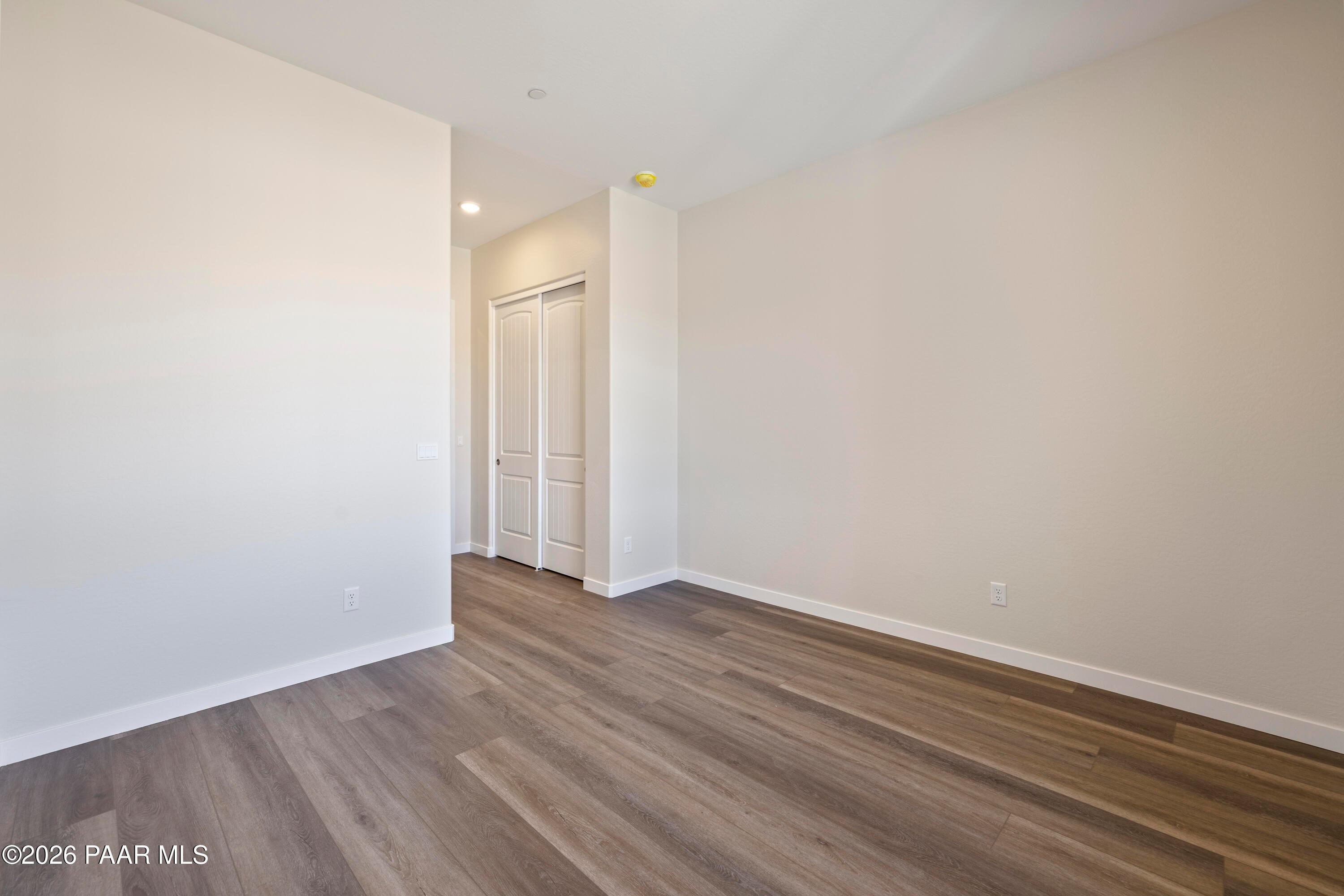 Spacious empty bedroom with sliding closet doors, beige walls, and luxury vinyl plank flooring in The Soleil E, Hidden Hills, Prescott, Arizona