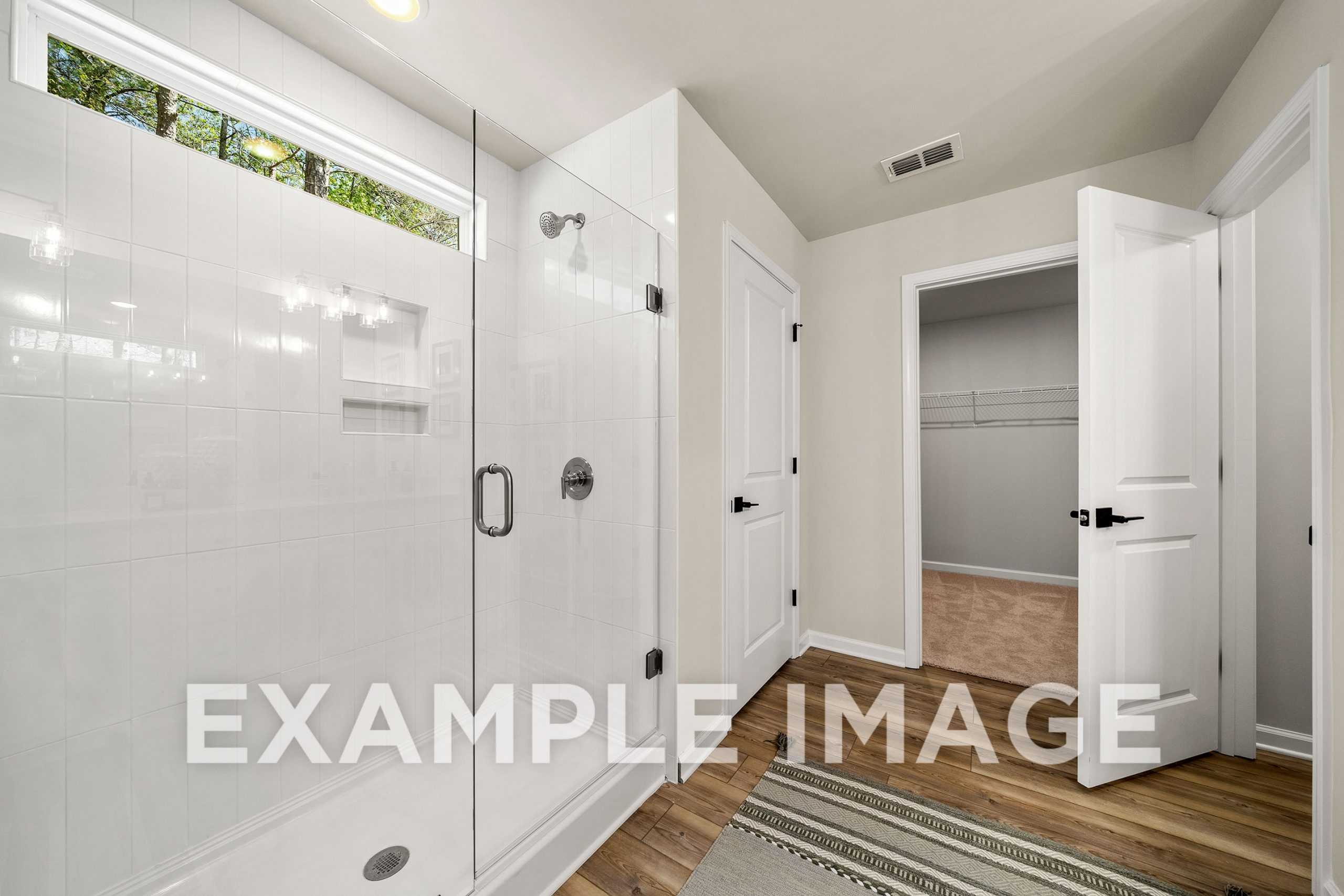 Spacious master bathroom in The Hickory A with frameless glass shower, white tiles, and open walk-in closet