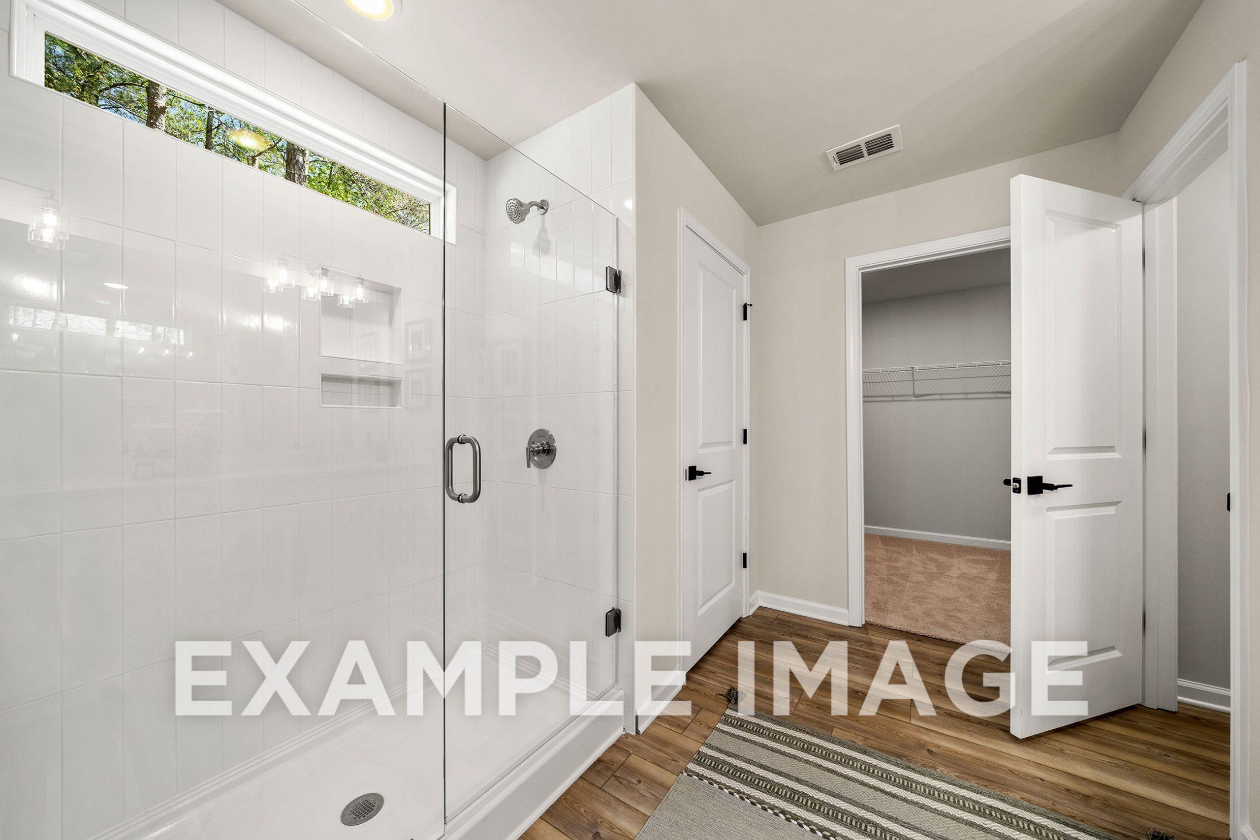 Modern master bathroom in The Hickory B featuring frameless glass shower, white subway tiles, and adjacent walk-in closet