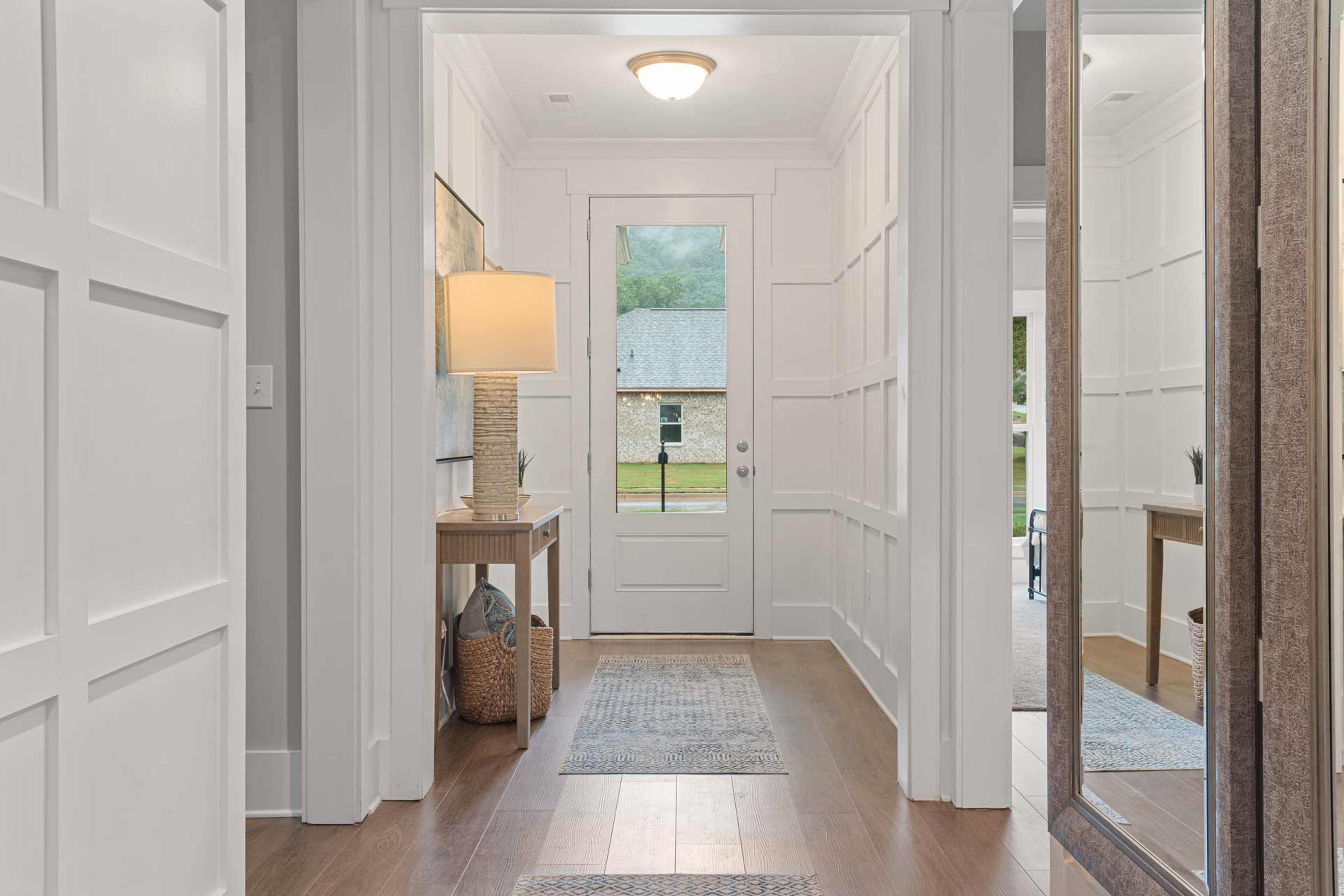 Bright entry hallway at Monteagle Cove in Owens Cross Roads AL with white wainscoting, hardwood floors, console table, and open front door