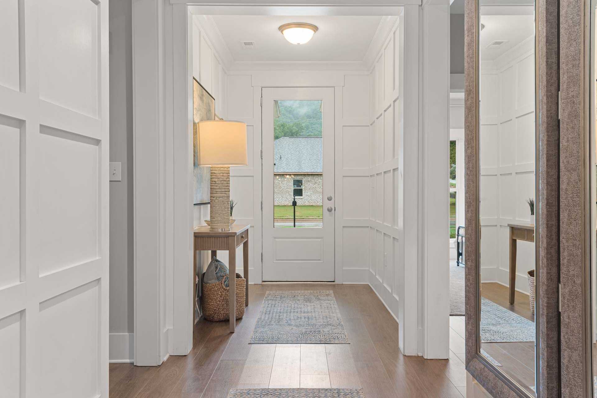 Bright entry hallway at Monteagle Cove in Owens Cross Roads AL with white wainscoting, hardwood floors, console table, and open front door