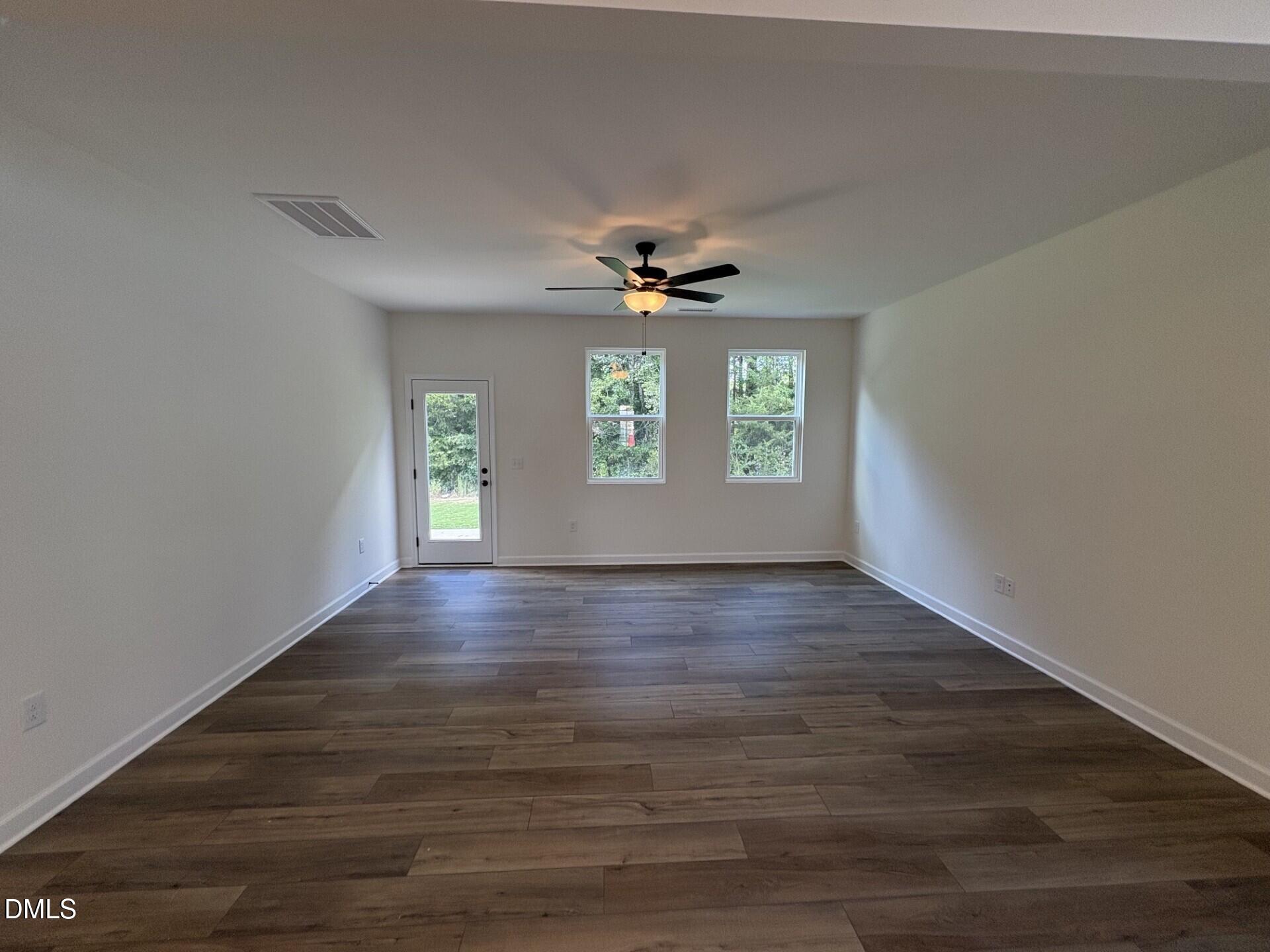 Bright empty living room with wood-look tile flooring, ceiling fan, and rear door in Davidson Homes The Adalynn A, Zebulon NC