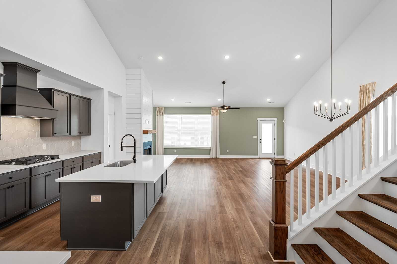 Modern kitchen with black cabinets, white quartz island, farmhouse sink, open to living area and wooden staircase in Davidson Homes The Ridgeport, Gallatin TN