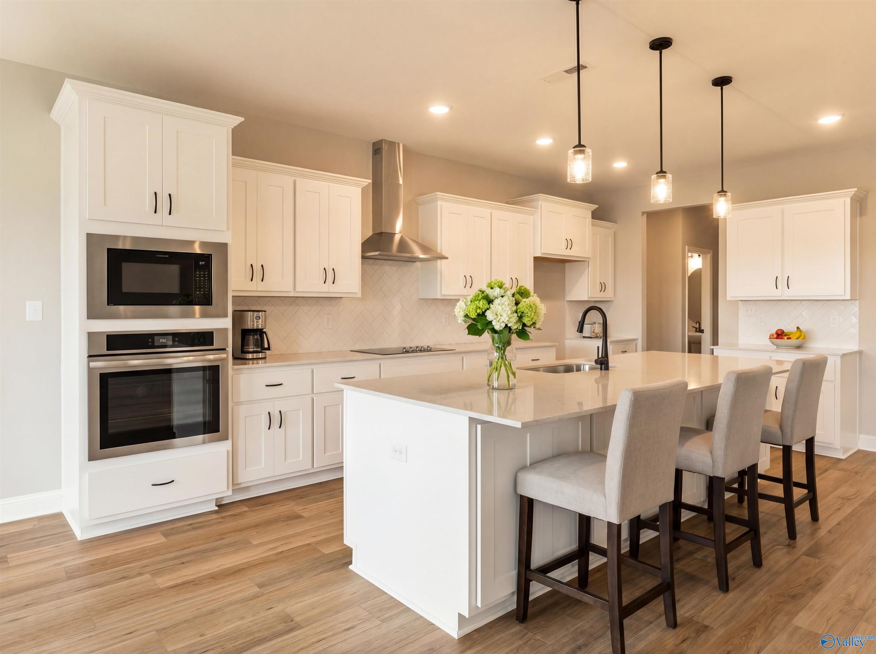 Modern white kitchen with quartz island, stainless oven, microwave, and bar stools in Davidson Homes The Finleigh, Toney, Alabama