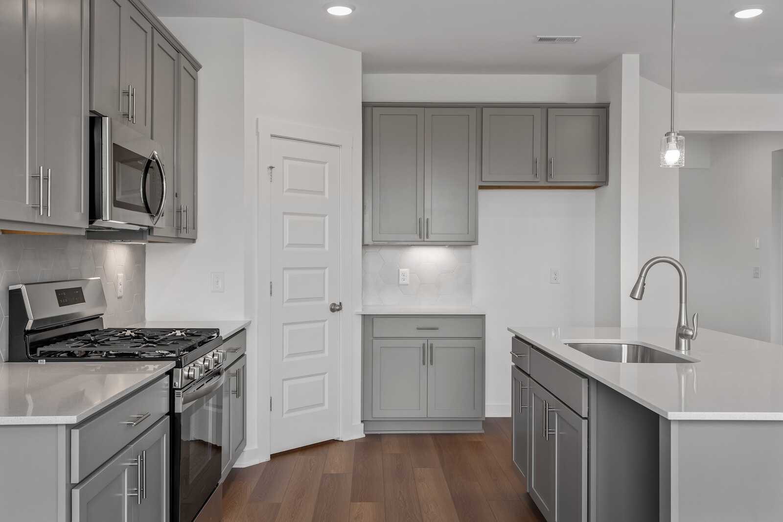 Modern kitchen in The Asheville by Davidson Homes featuring gray shaker cabinets, white quartz island with sink, stainless steel appliances, hardwood floors