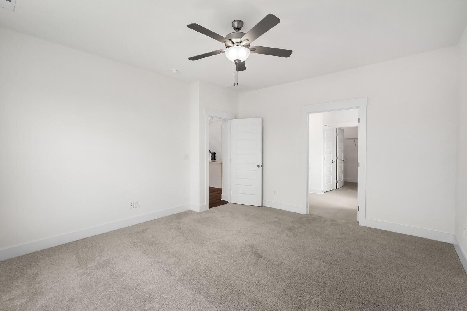 Spacious bedroom with ceiling fan, white walls, carpet floor, and adjacent doors in Davidson Homes The Ridgeport, Gallatin, TN