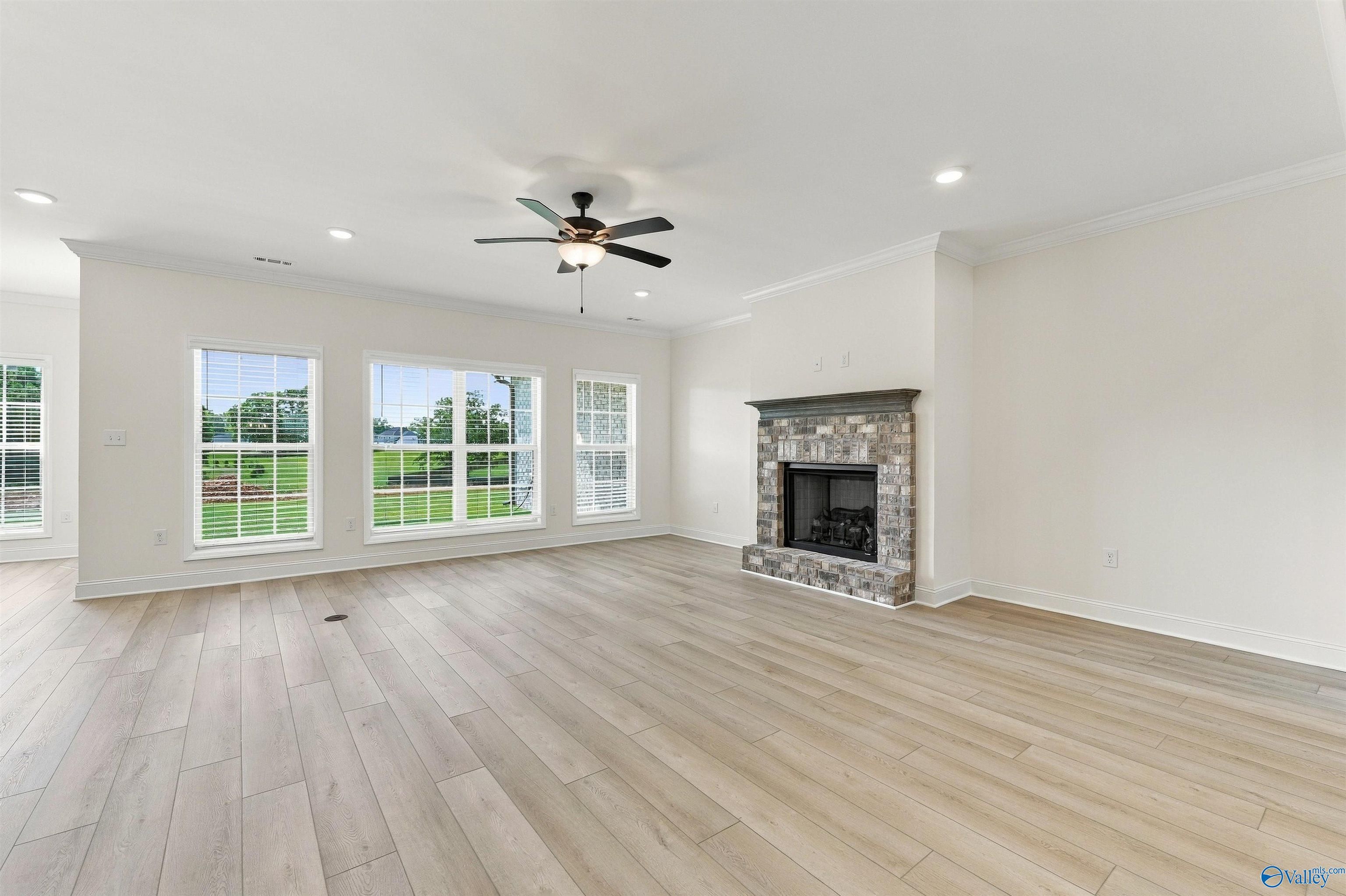 Bright living room with brick fireplace, wood-look tile floors, and backyard windows in Davidson Homes' The Valencia, Huntsville, AL
