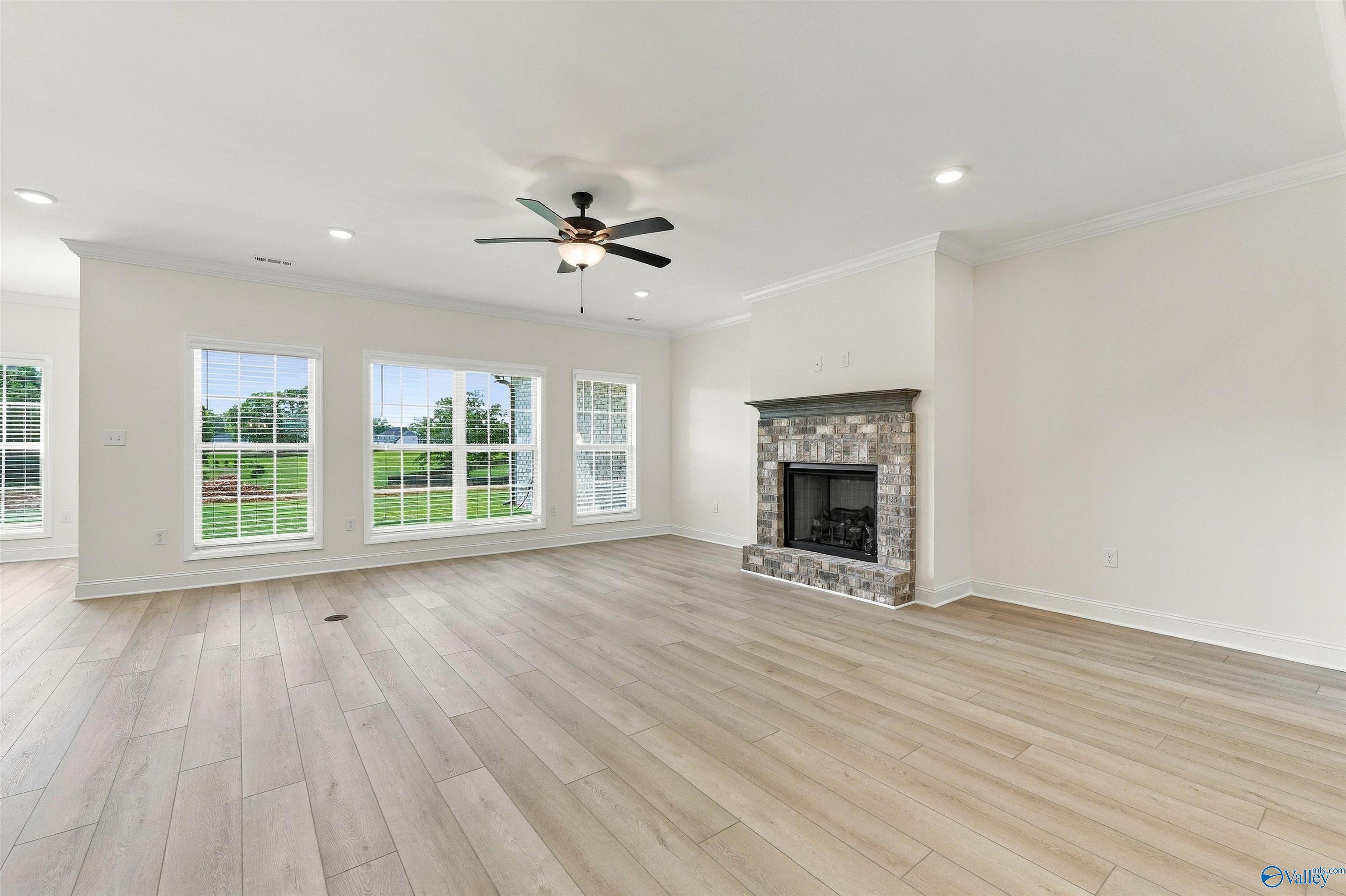 Bright living room with brick fireplace, wood-look tile floors, and backyard windows in Davidson Homes' The Valencia, Huntsville, AL
