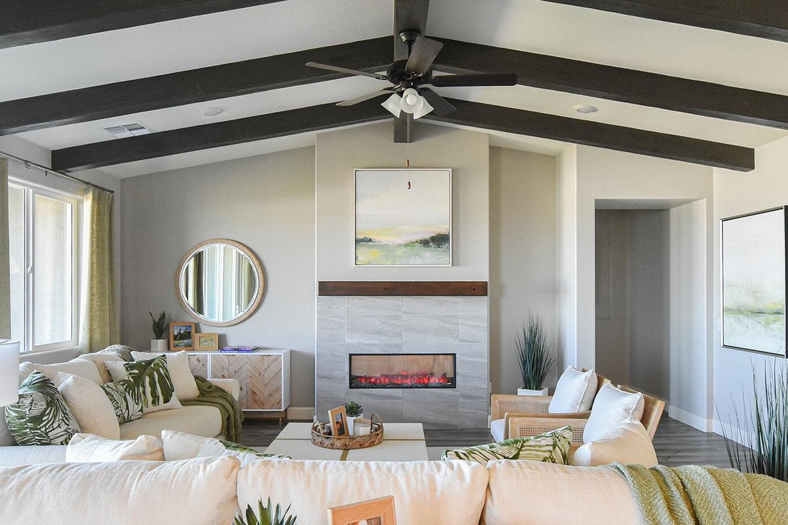 Spacious living room in The Summit E featuring vaulted beam ceiling, stone gas fireplace, modern sofa, and abstract art