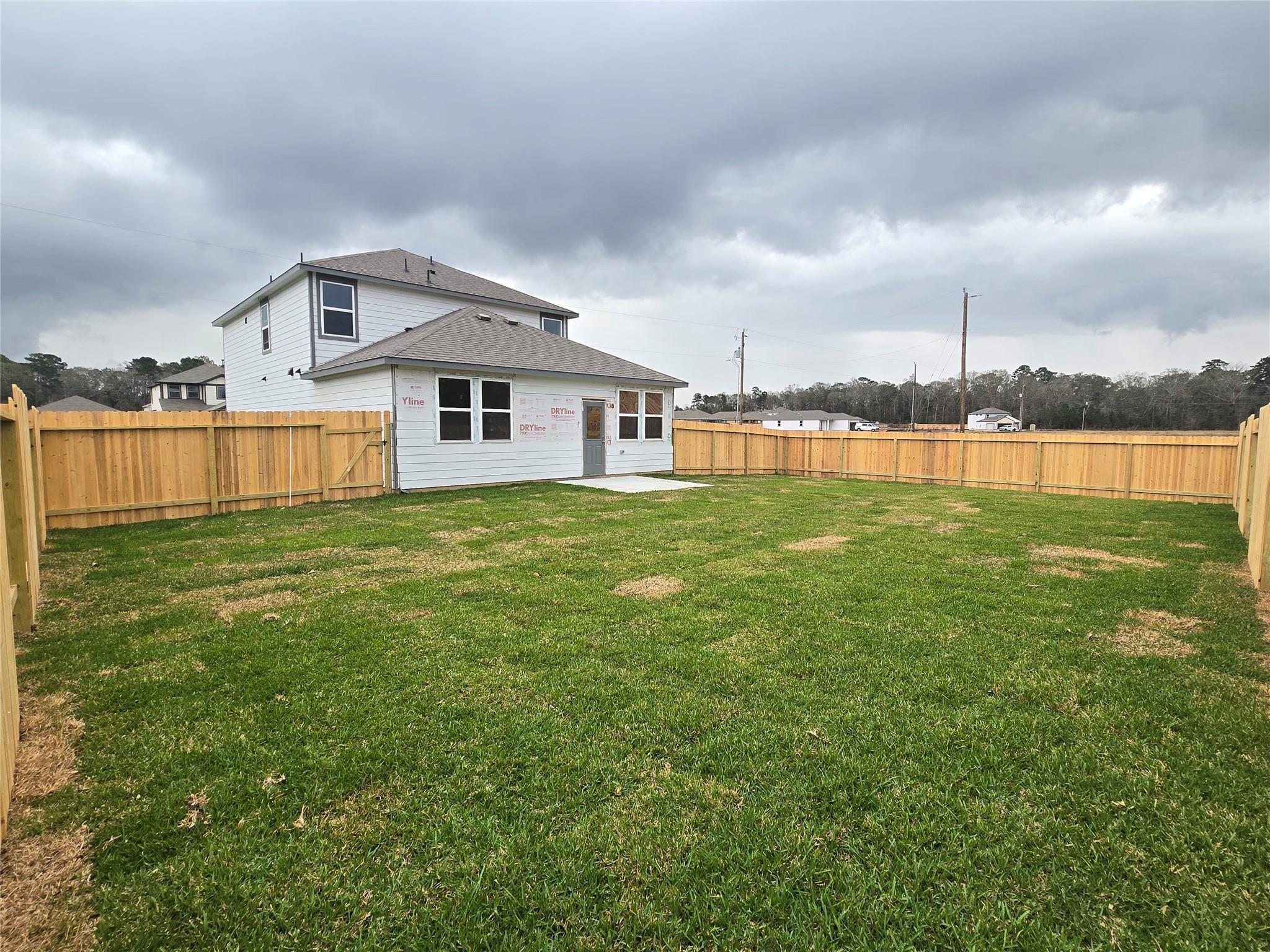 Two-story white home with spacious fenced grassy backyard under cloudy sky in Liberty Estates, Cleveland, Texas