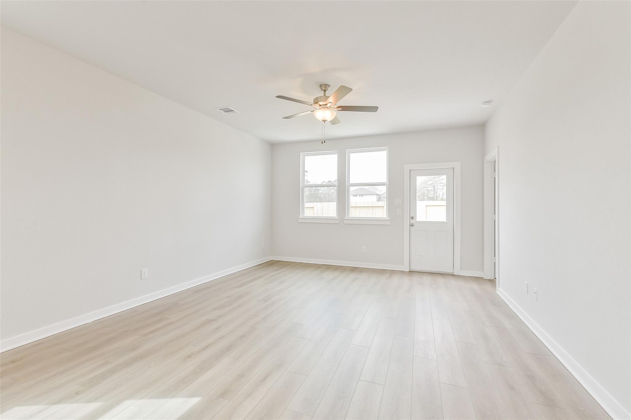 Bright empty bedroom with light wood floors, white walls, ceiling fan, and large windows in The Frio G home, Cleveland, Texas