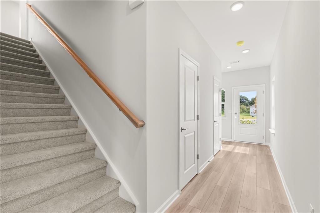 Bright entryway with wood-look flooring and carpeted stairs in The Russell A floor plan at Cedar Farms, Winder, Georgia.
