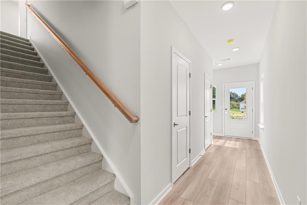 Bright entryway with wood-look flooring and carpeted stairs in The Russell A floor plan at Cedar Farms, Winder, Georgia.
