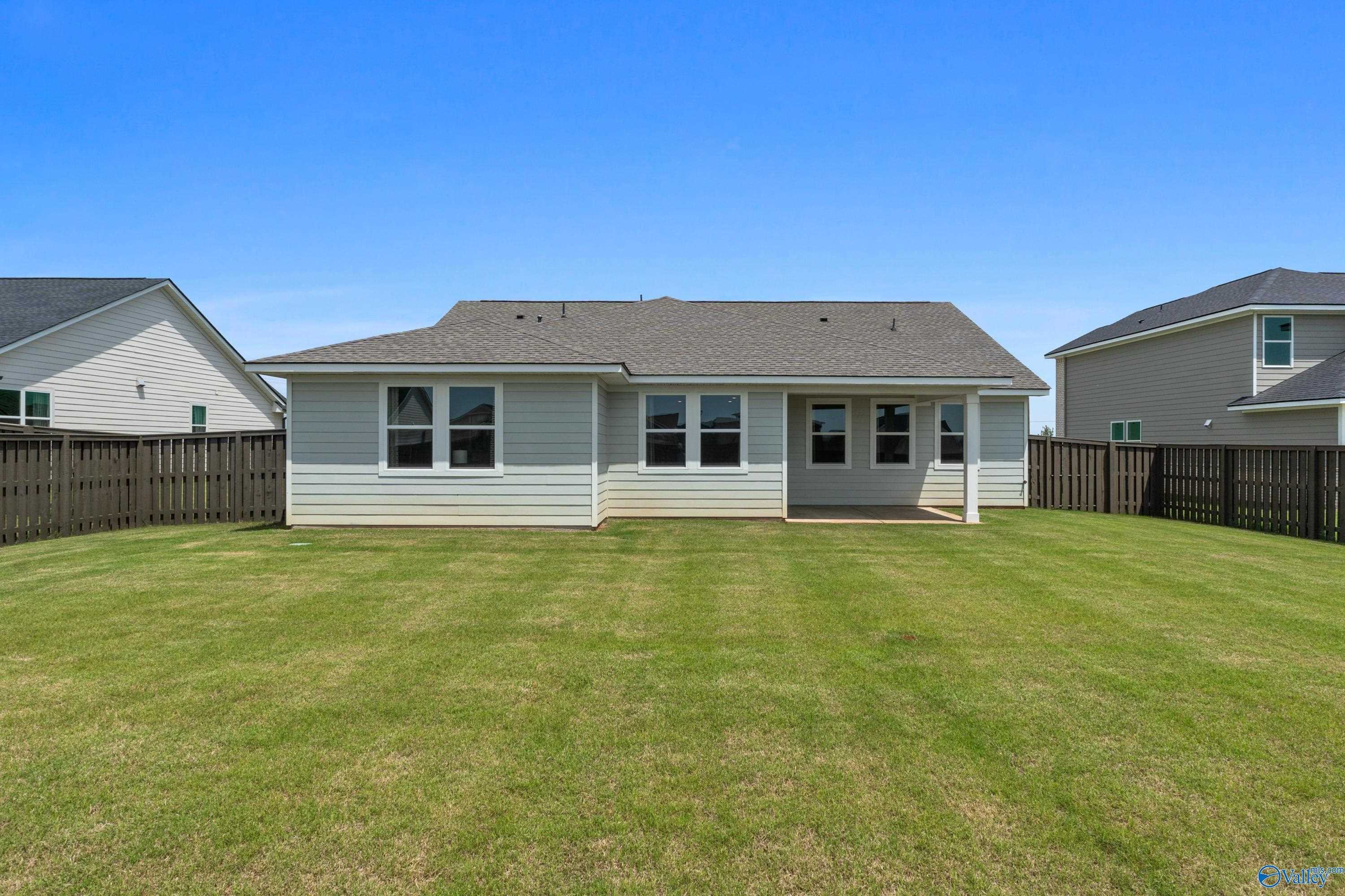 Rear view of single-story 4-bedroom home with covered patio, large grassy backyard and privacy fence in Anderson Farm, Athens, Alabama