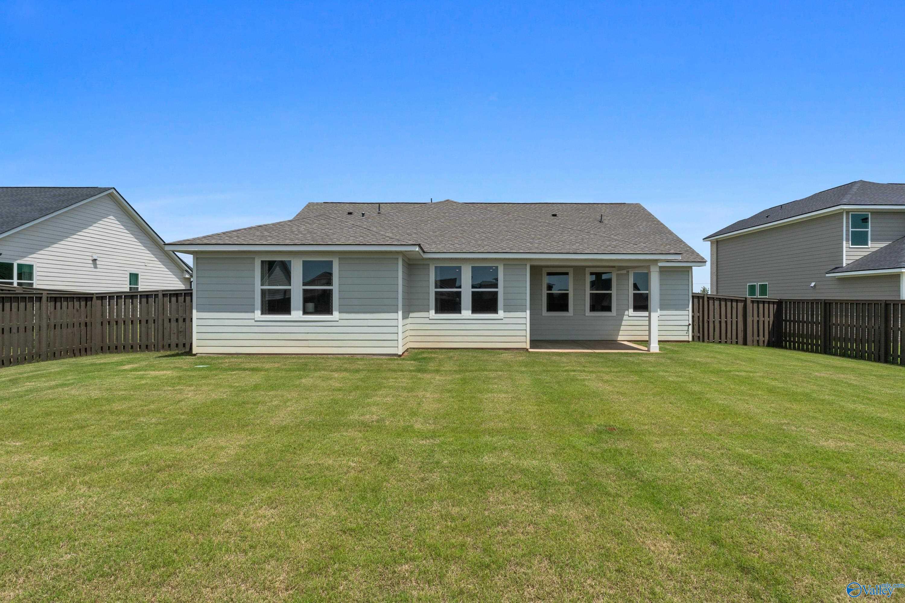 Rear view of single-story 4-bedroom home with covered patio, large grassy backyard and privacy fence in Anderson Farm, Athens, Alabama