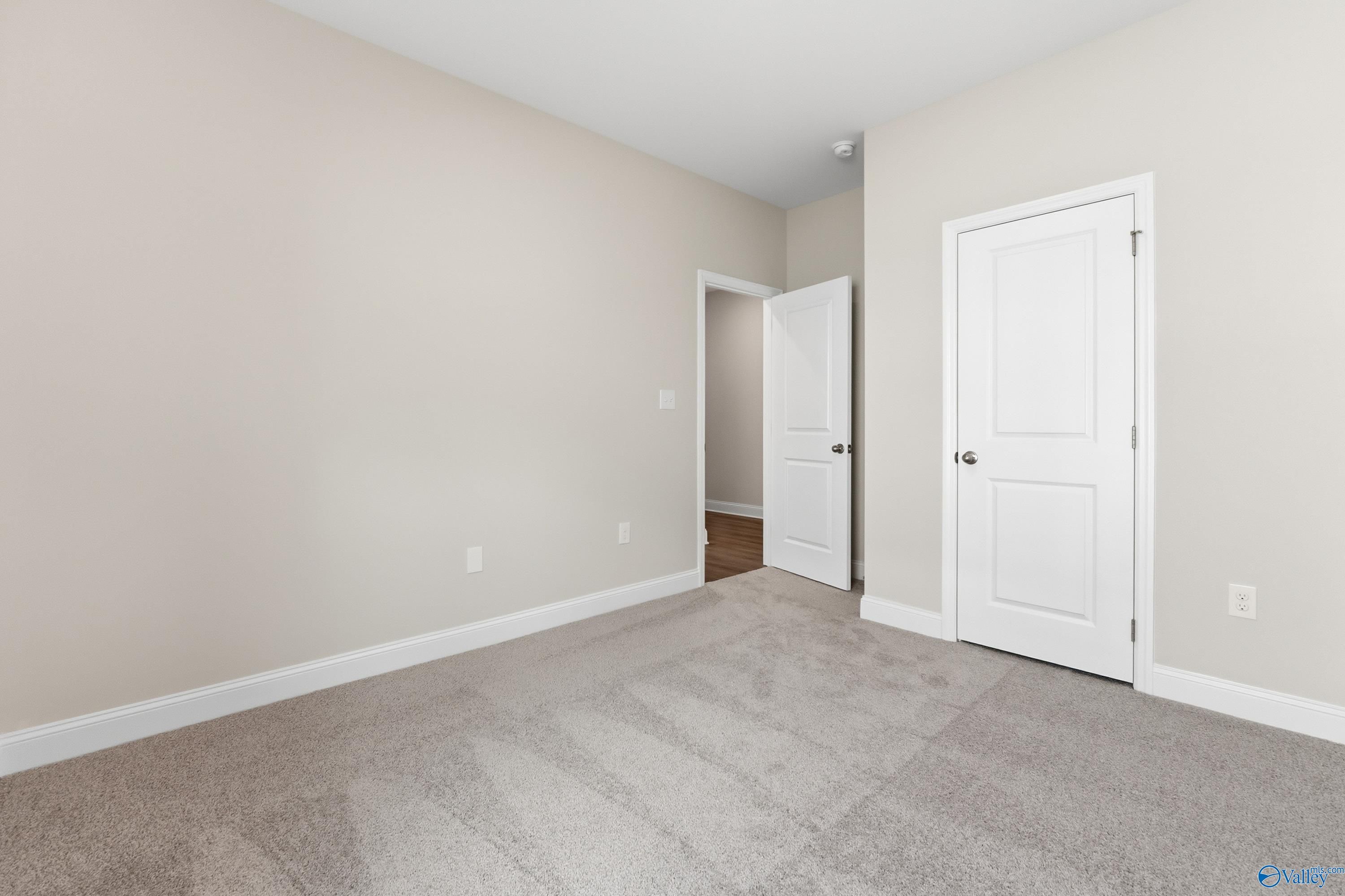 Empty secondary bedroom featuring beige walls, gray carpet, and white doors in Davidson Homes The Asheville C, Huntsville, AL