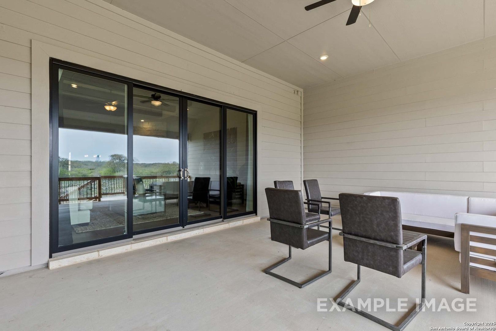 Covered patio with sliding glass doors, ceiling fan, and outdoor seating overlooking green backyard in Davidson Homes The Summerlin B, Castroville, Texas