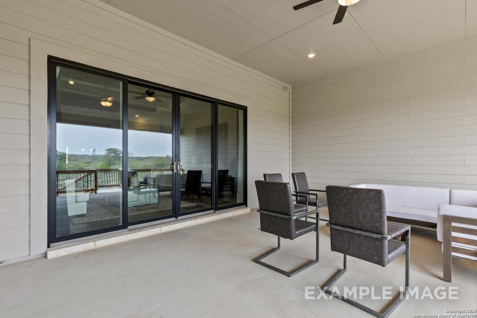 Covered patio with sliding glass doors, ceiling fan, and outdoor seating overlooking green backyard in Davidson Homes The Summerlin B, Castroville, Texas