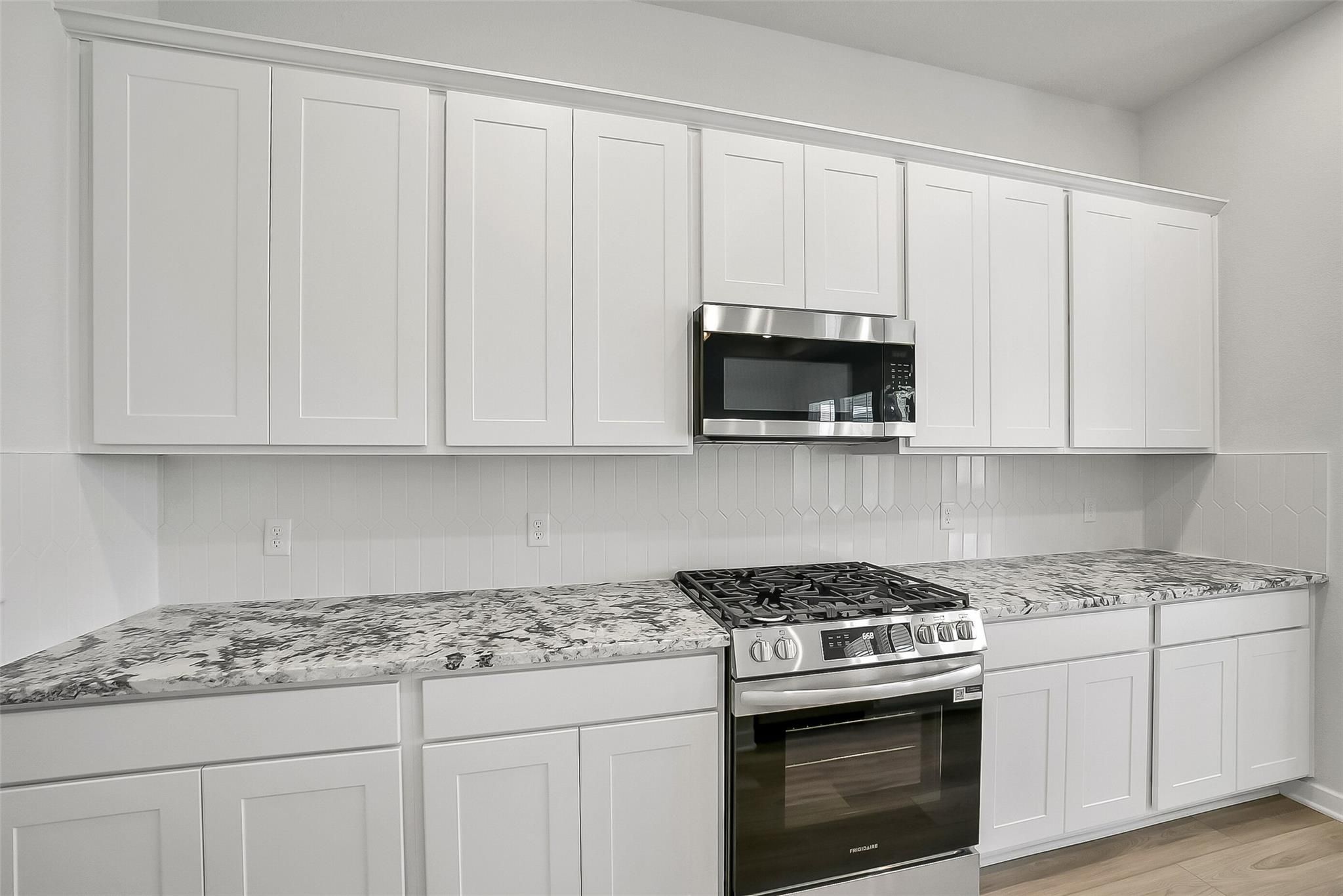 Modern white shaker kitchen with granite countertops, gas cooktop, stainless appliances in Davidson Homes The Acadia A, Katy, Texas