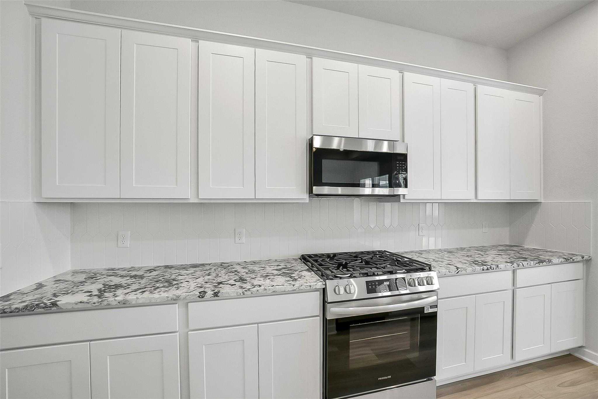 Modern white shaker kitchen with granite countertops, gas cooktop, stainless appliances in Davidson Homes The Acadia A, Katy, Texas