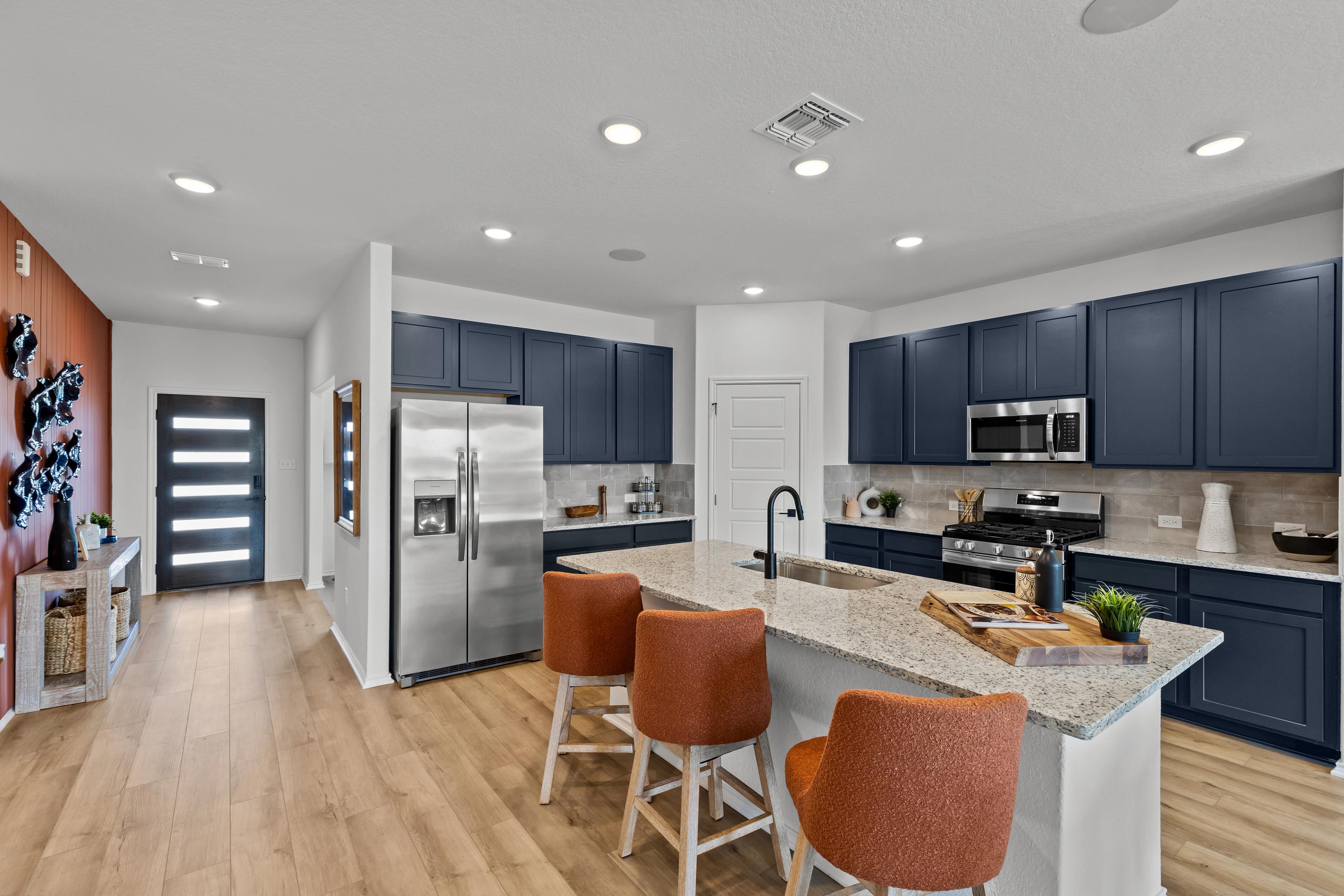 Modern navy kitchen in The Douglas F with large quartz island, stainless appliances, orange bar stools, hardwood floors