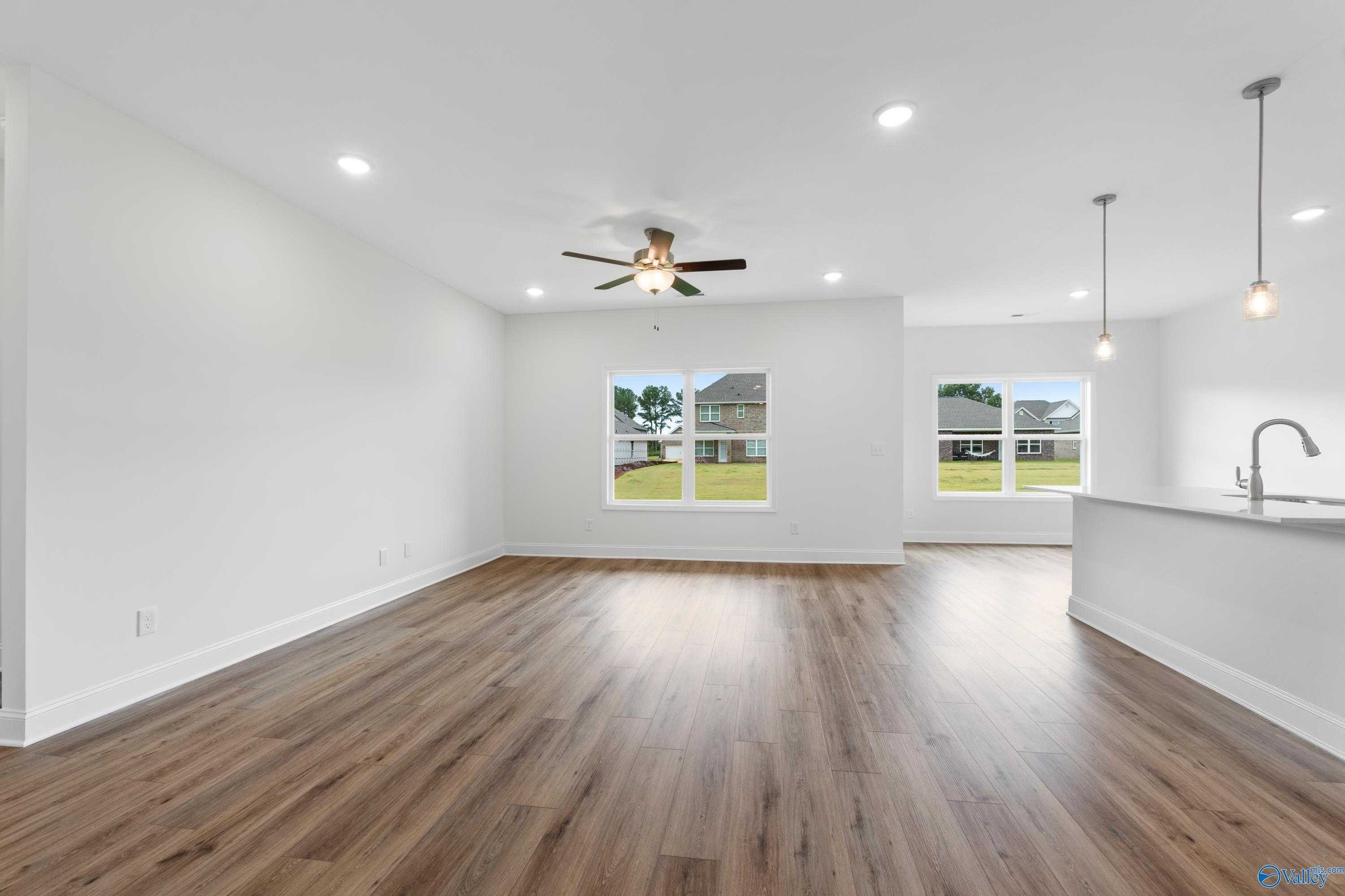 Open-concept living room with hardwood floors, ceiling fan, and large windows to backyard in Davidson Homes The Asheville C, Athens AL