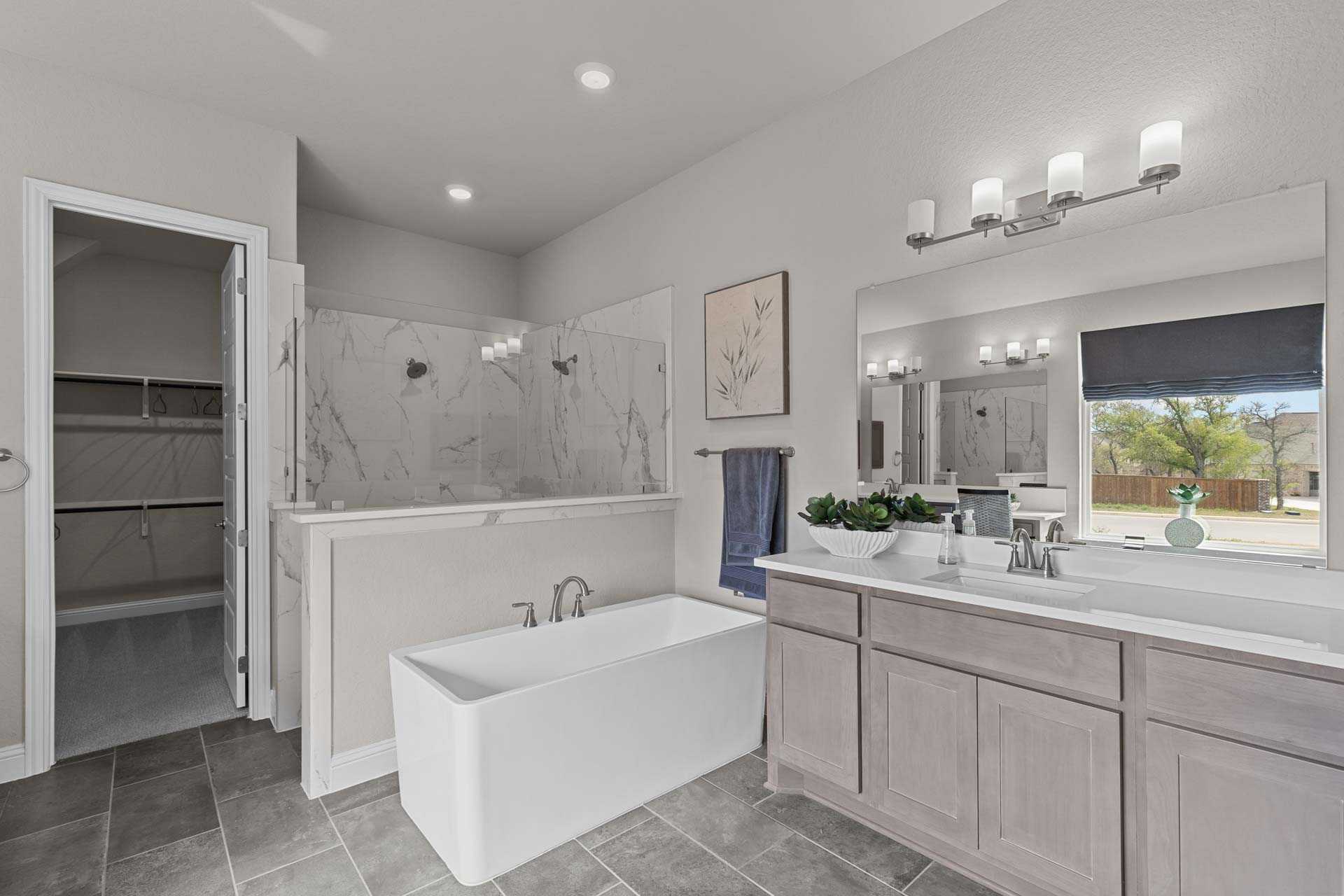 Luxurious master bathroom in The Garner A showcasing freestanding white tub, marble walk-in shower, double gray vanity, and closet