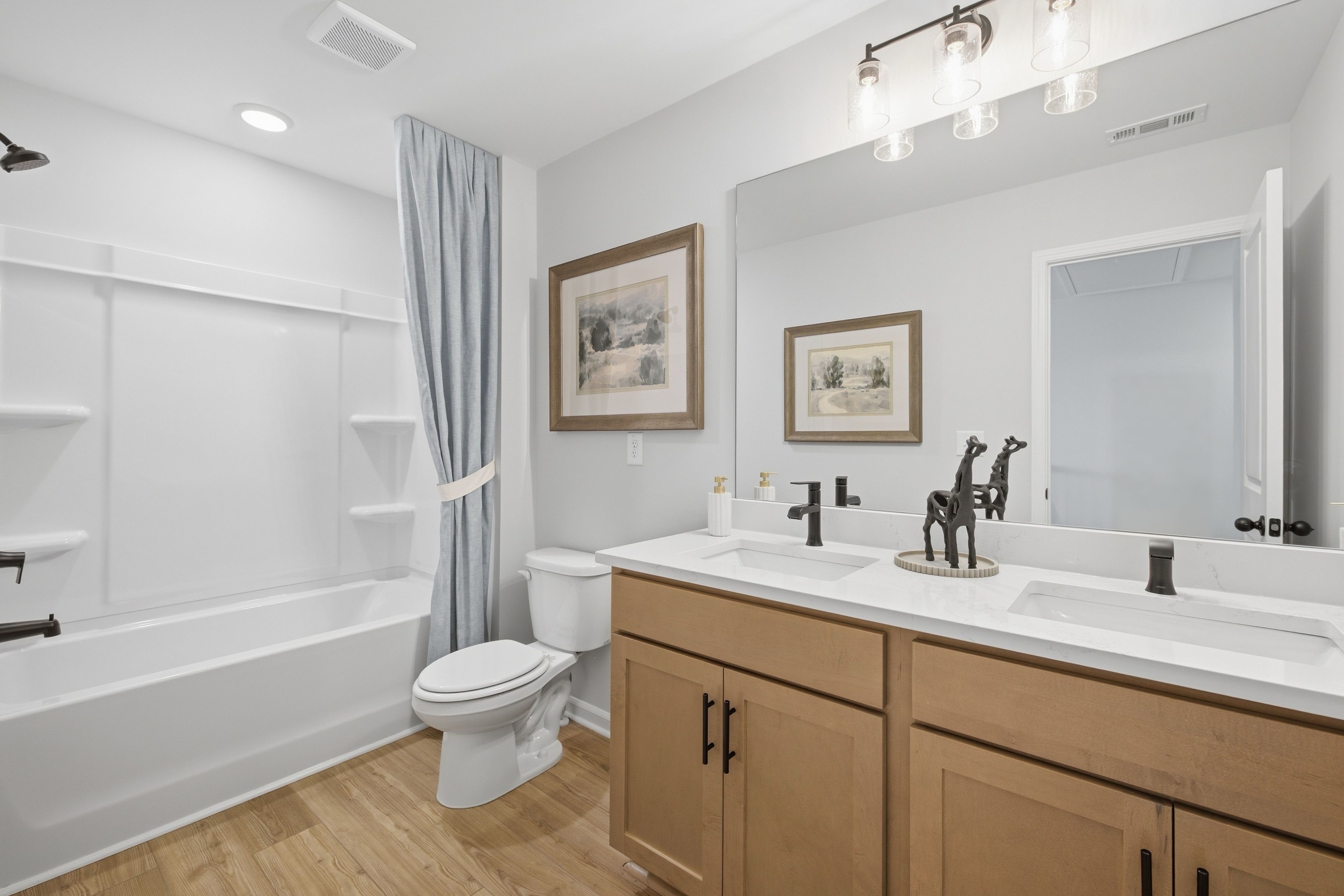 Modern bathroom at Greene Farm in Cartersville, Georgia with dual vanity, wood cabinets, and tub shower combo by Davidson Homes