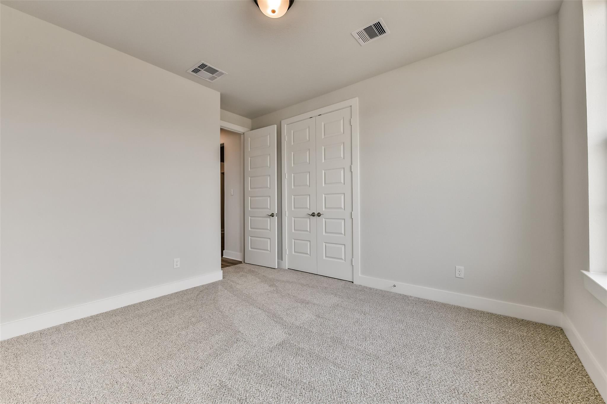 Empty secondary bedroom with double closet doors, neutral carpet, and ample natural light in Davidson Homes The George A, Texas City
