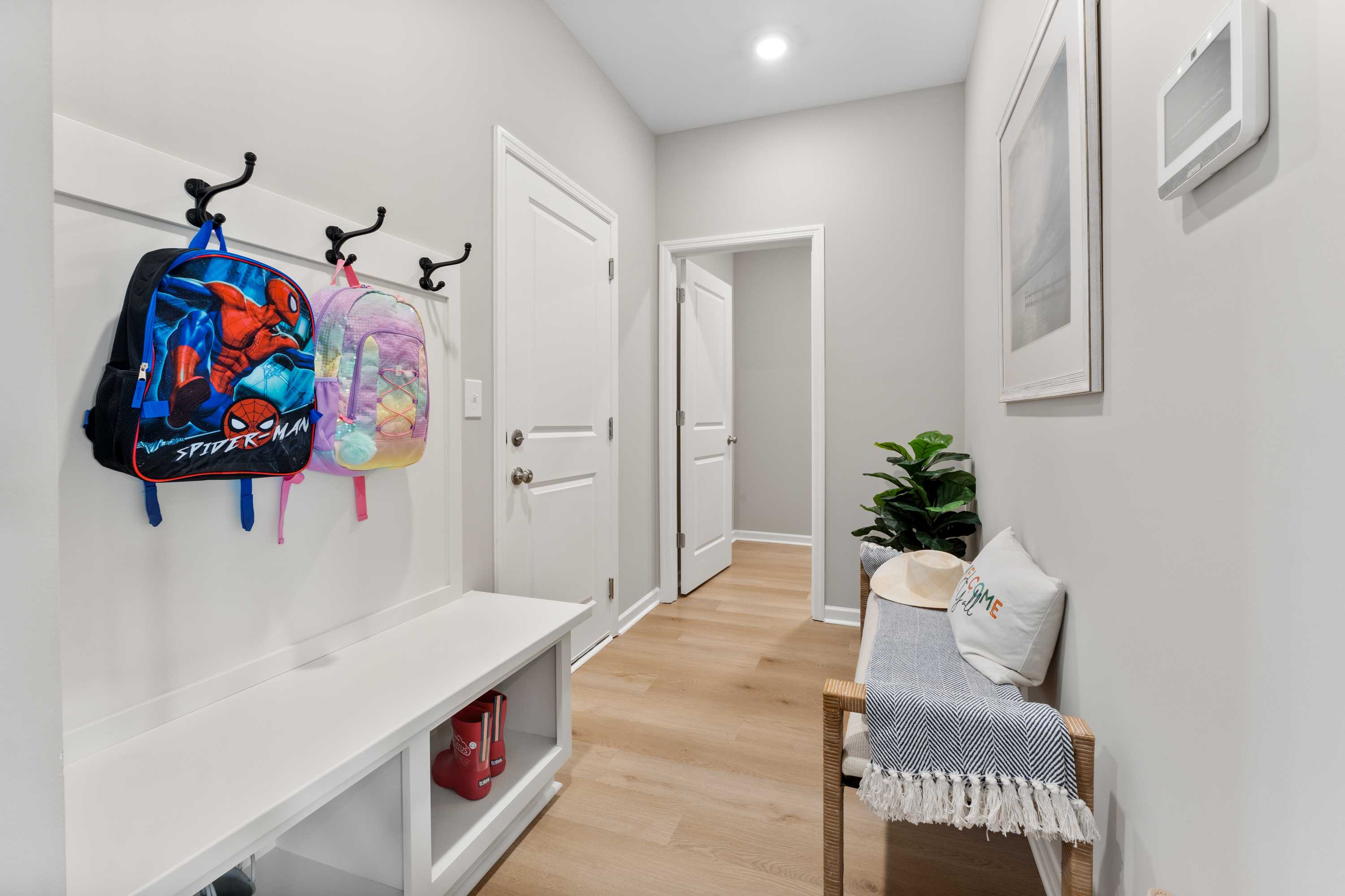 Family-friendly mudroom at Forest Glen in Hazel Green Alabama with kids backpacks on hooks white bench and potted plant