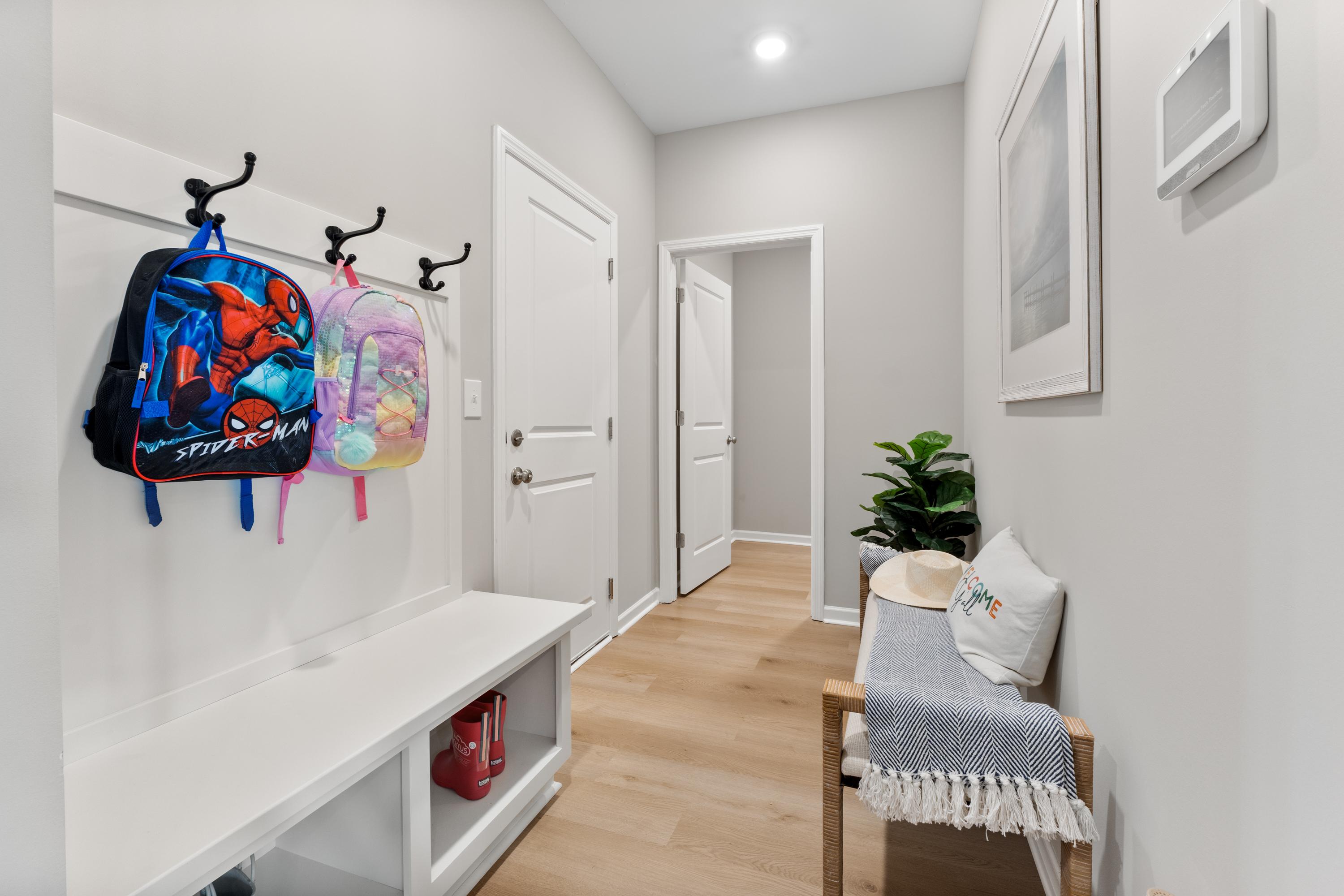 Family-friendly mudroom at Forest Glen in Hazel Green Alabama with kids backpacks on hooks white bench and potted plant