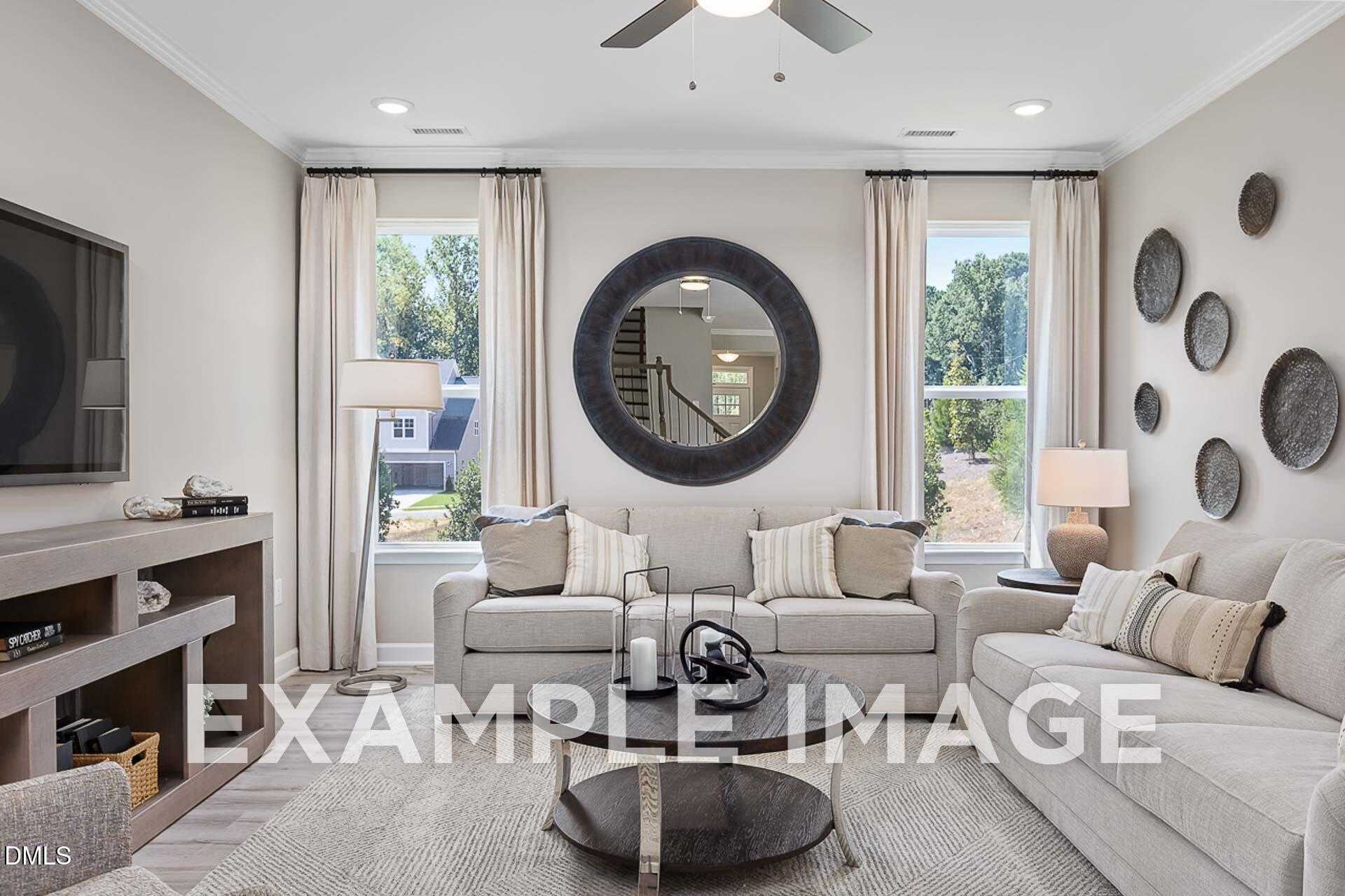 Modern living room with beige sofa, large round mirror, TV console, and ceiling fan in Davidson Homes The Ash B, Lillington, NC