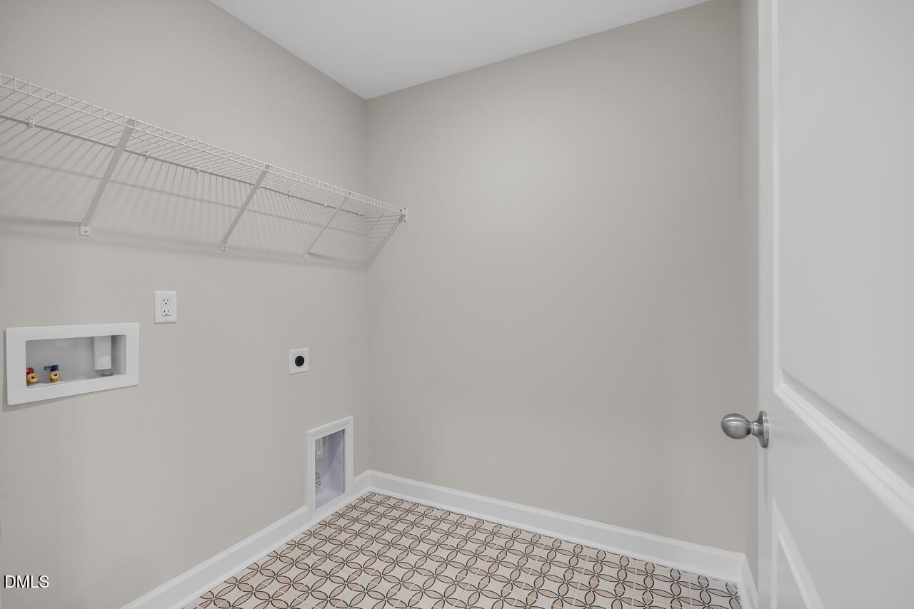 Functional laundry room with wire shelving, washer-dryer hookups, pet door, and patterned tile in Davidson Homes The Avery, Knightdale, NC
