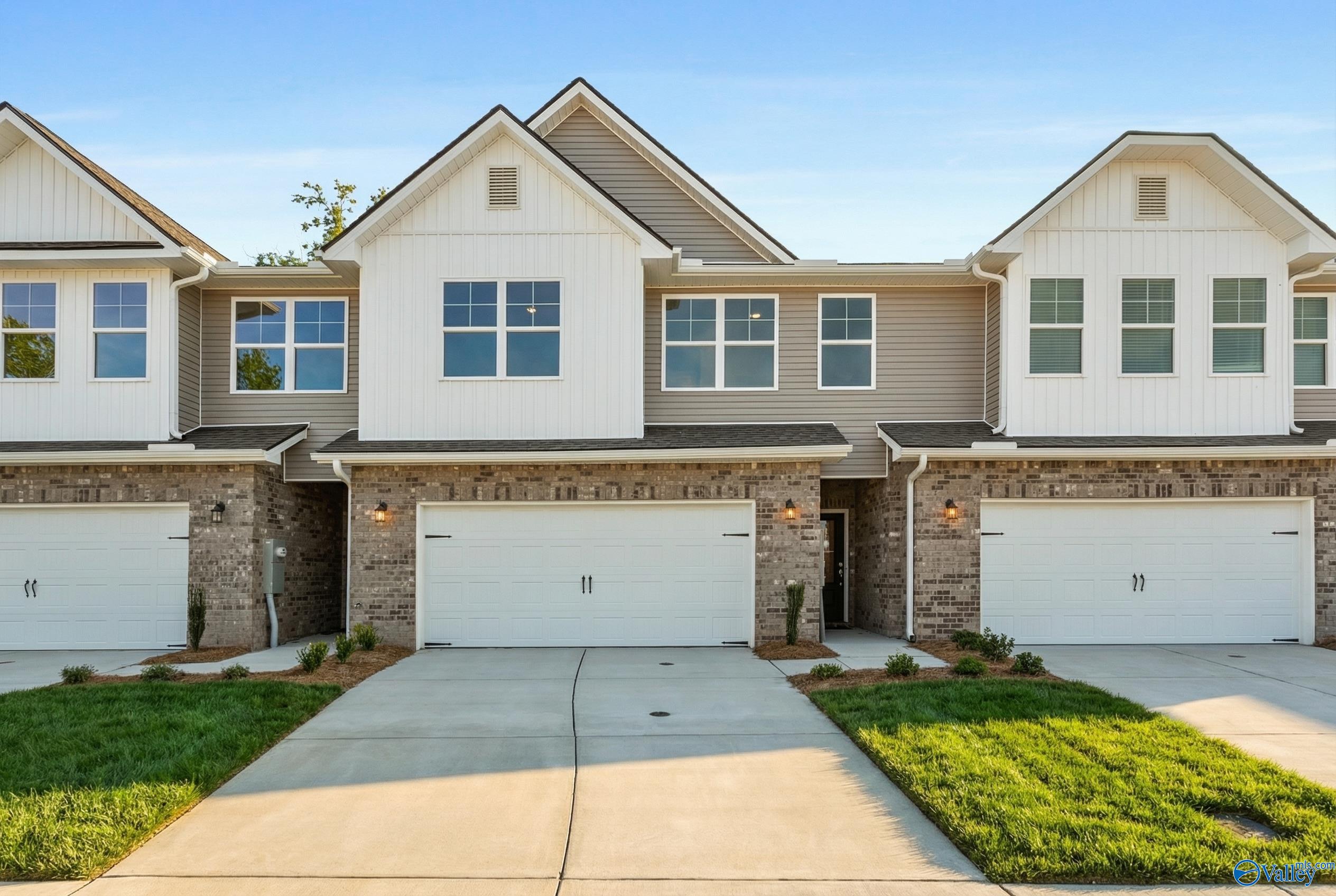Row of three modern 2-story townhomes with 2-car garages, white siding and brick accents in Pavilion, Huntsville, Alabama by Davidson Homes