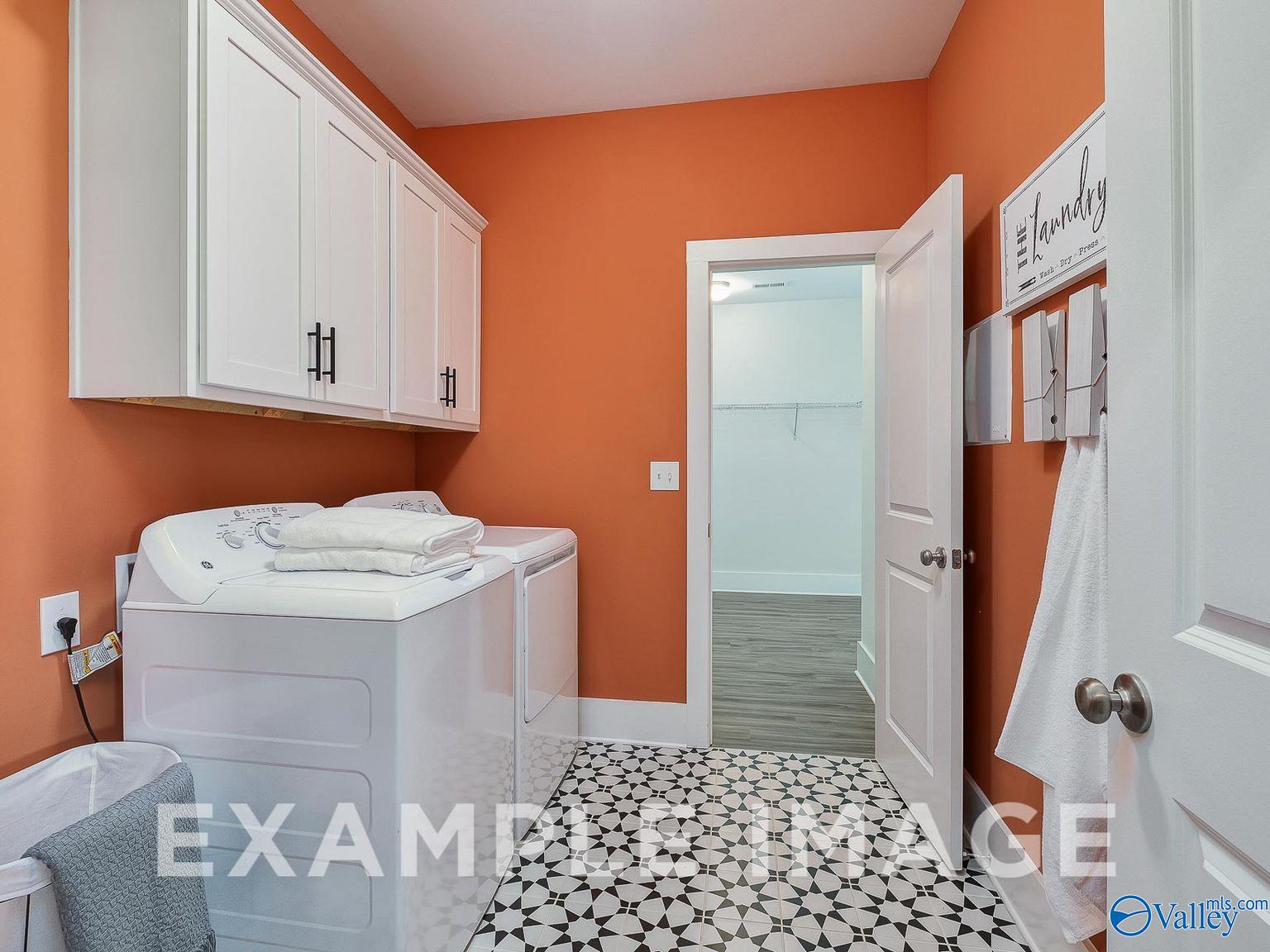 Modern laundry room featuring white washer-dryer set, upper cabinets, and orange walls in Davidson Homes The Everett B, Toney, Alabama