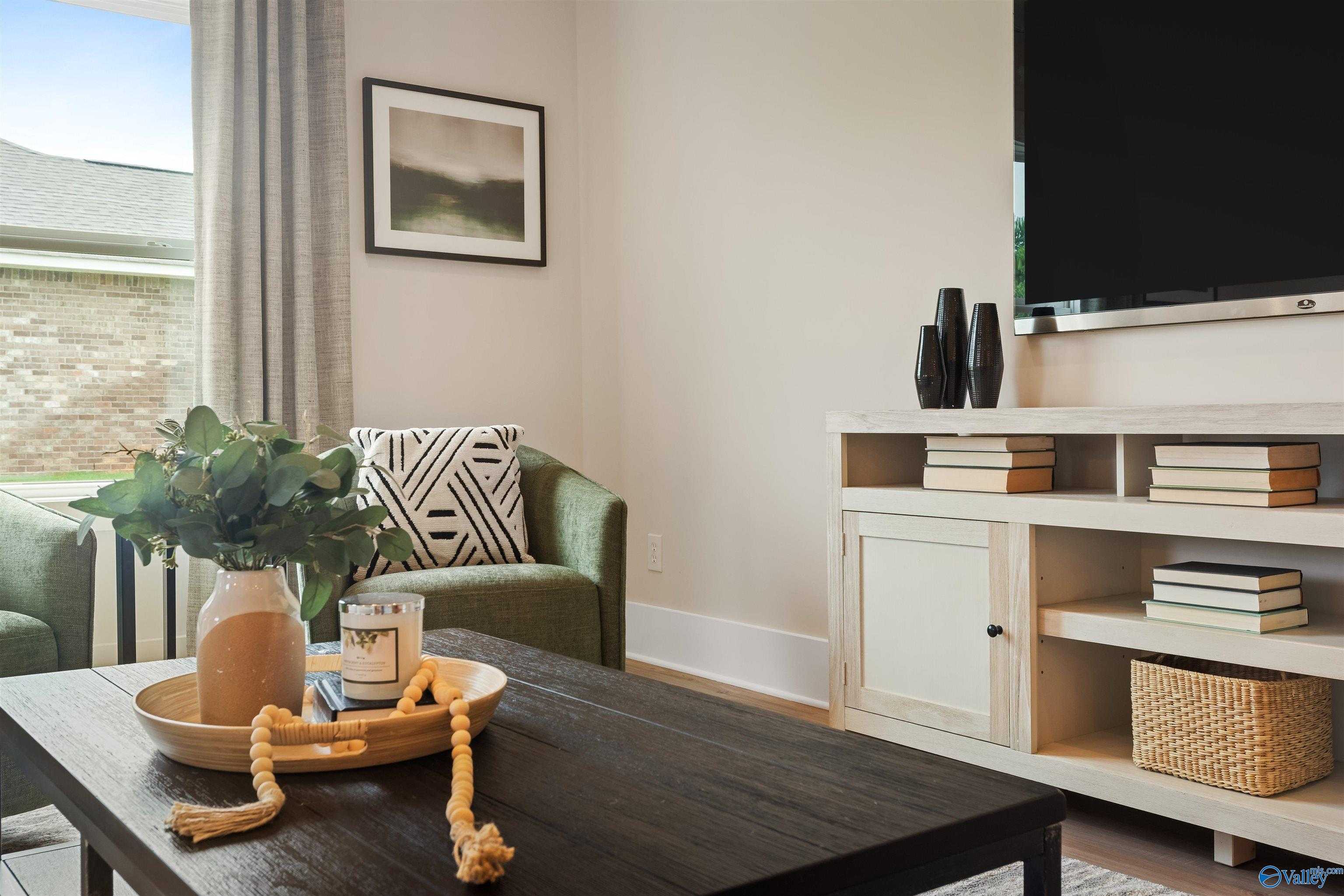 Cozy living room with mounted TV, geometric green armchair, eucalyptus vase, and black coffee table in Davidson Homes The Daphne, Harvest, Alabama