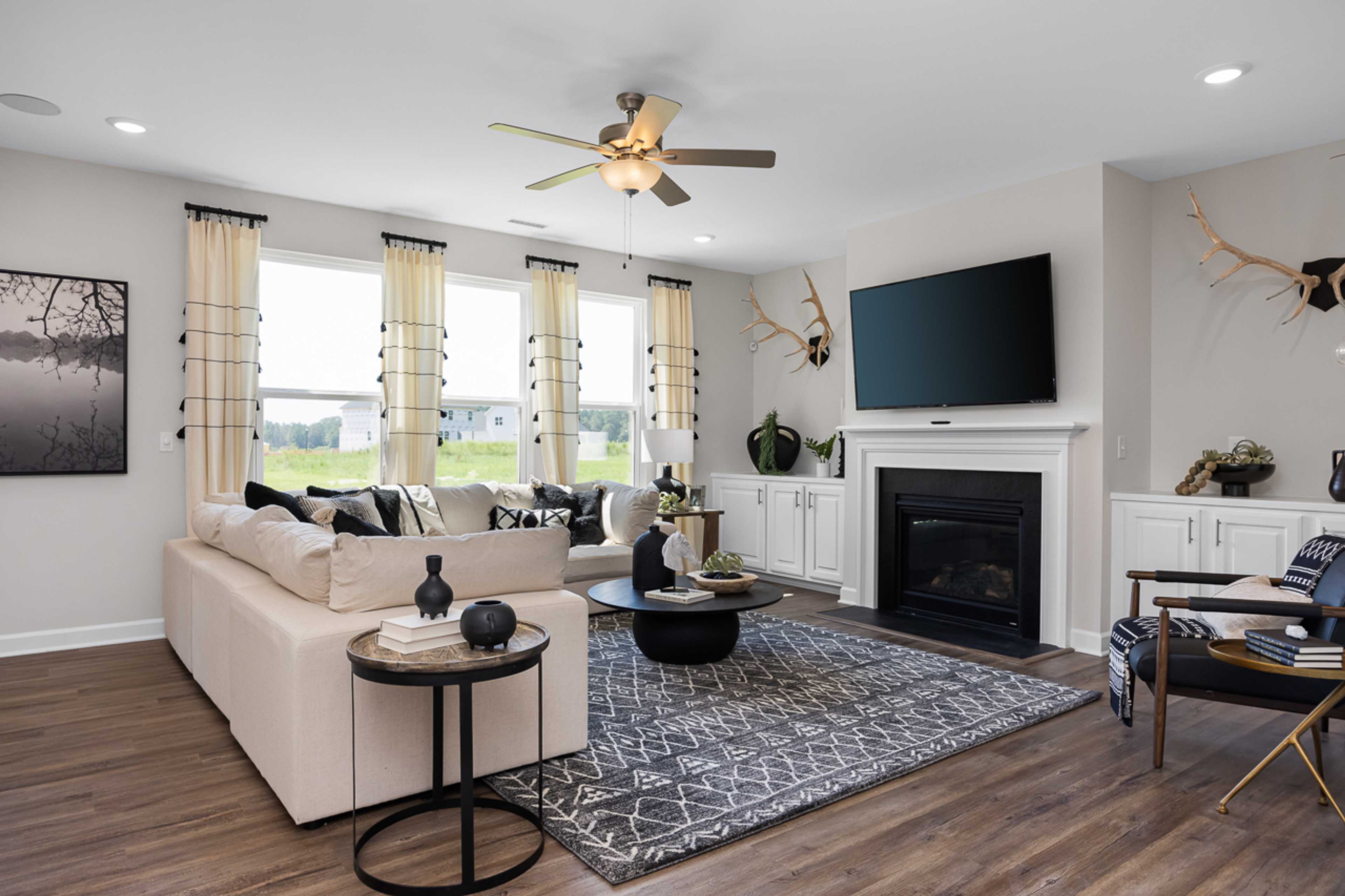 Spacious living room at Wellers Knoll in Lillington NC with beige sectional sofa, gas fireplace, mounted TV, and hardwood floors