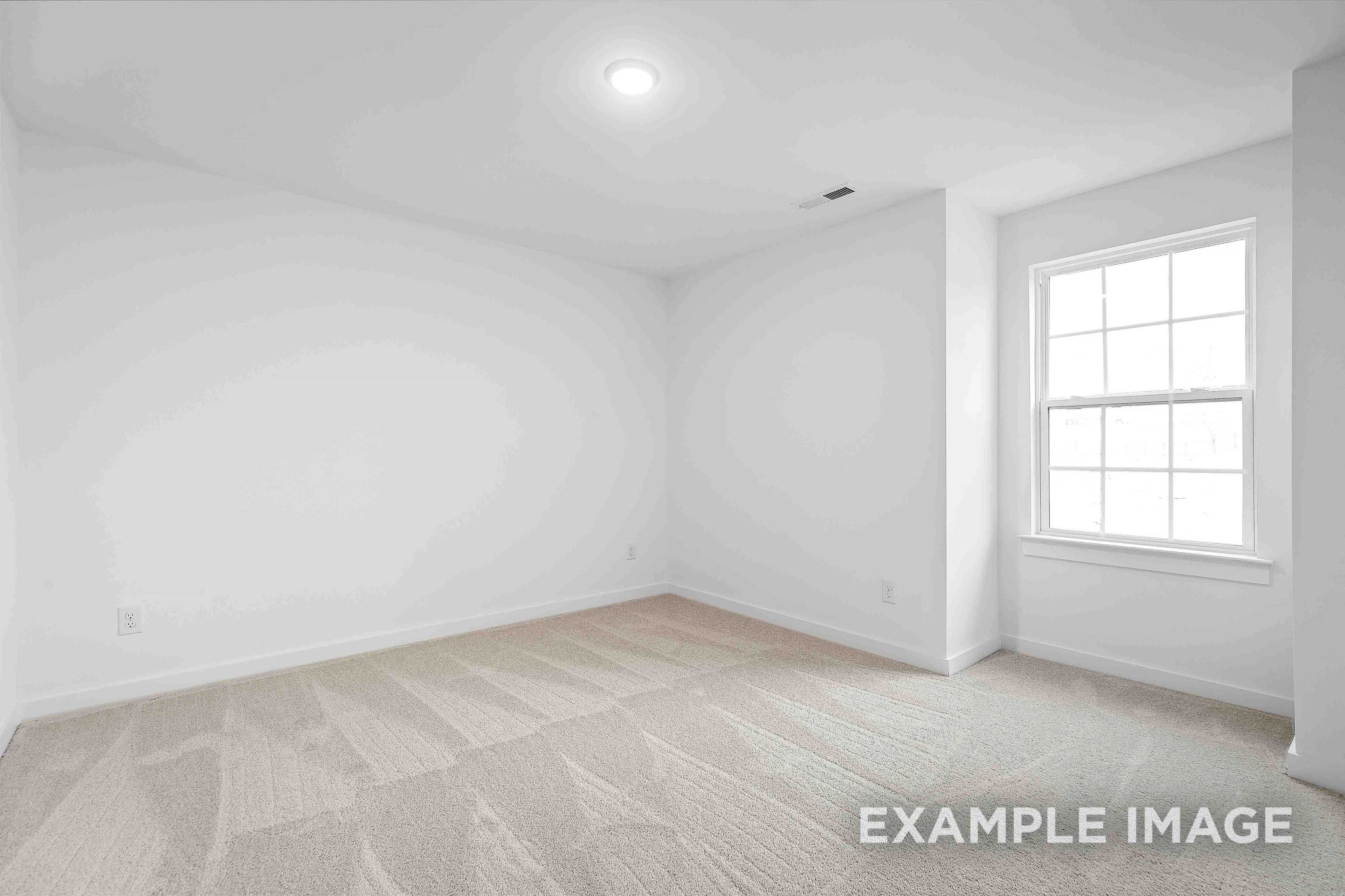 Spacious empty bedroom in The Charleston home with white walls, large window, and beige carpet