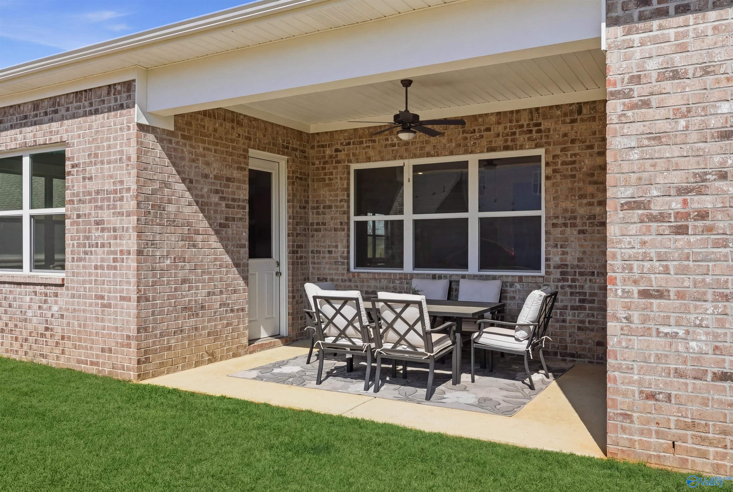 Covered patio with wicker dining set, ceiling fan, and lush green lawn in 5-bedroom Evermore Homes The Oxford B, Owens Cross Roads, Alabama