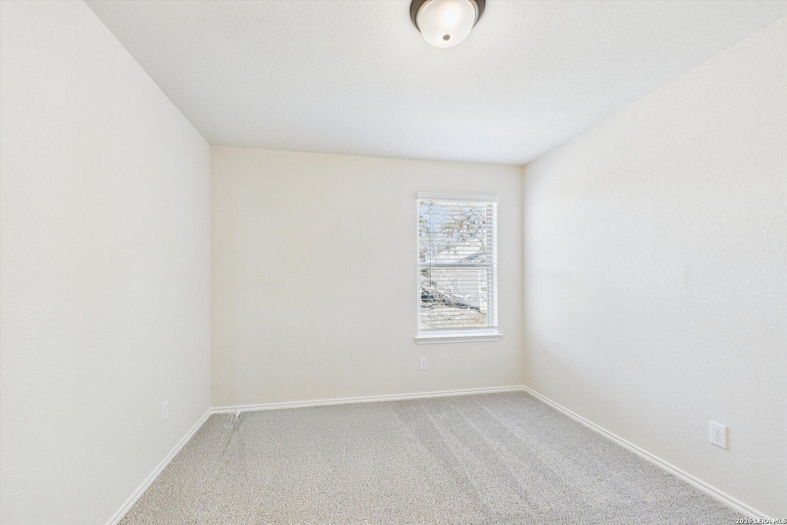 Bright secondary bedroom with beige walls, gray carpet, and window in Davidson Homes The Gillian B, San Antonio