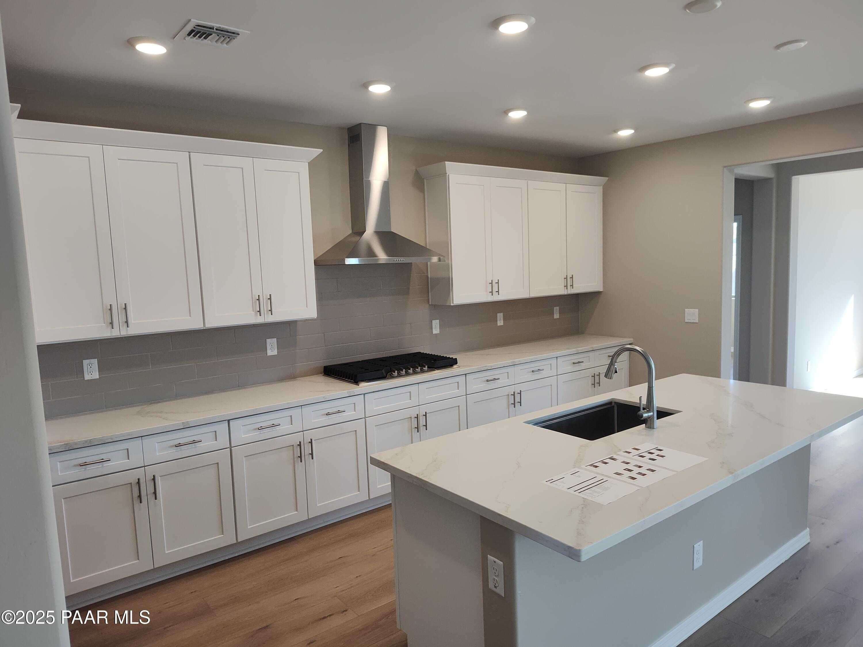 Modern white shaker kitchen with quartz island, stainless gas range, and recessed lighting in Davidson Homes Inspiration A, Prescott Valley AZ