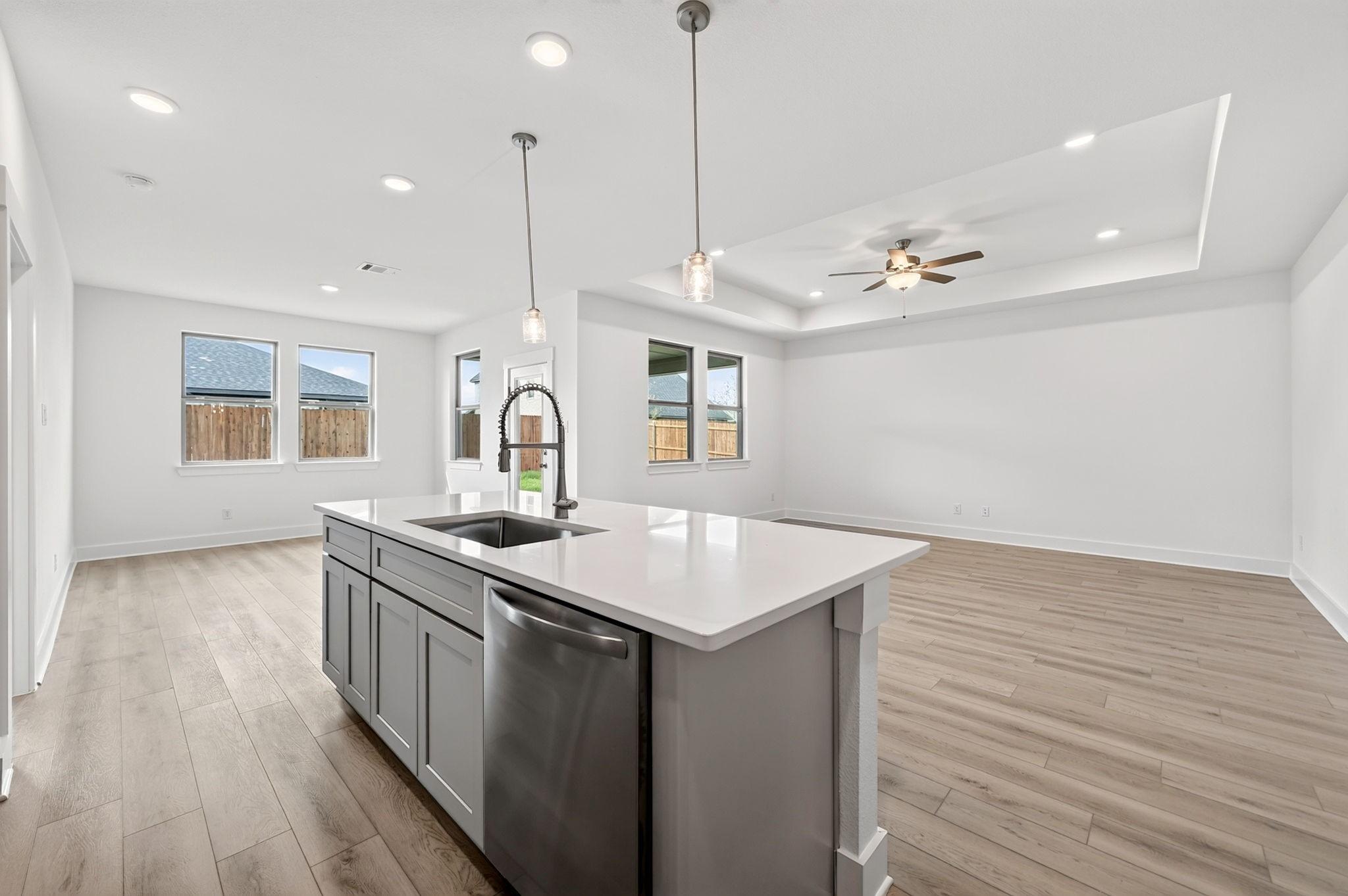 Open-concept kitchen with gray island, white quartz countertops, and luxury vinyl plank flooring in Davidson Homes The Holly F, Josephine, TX
