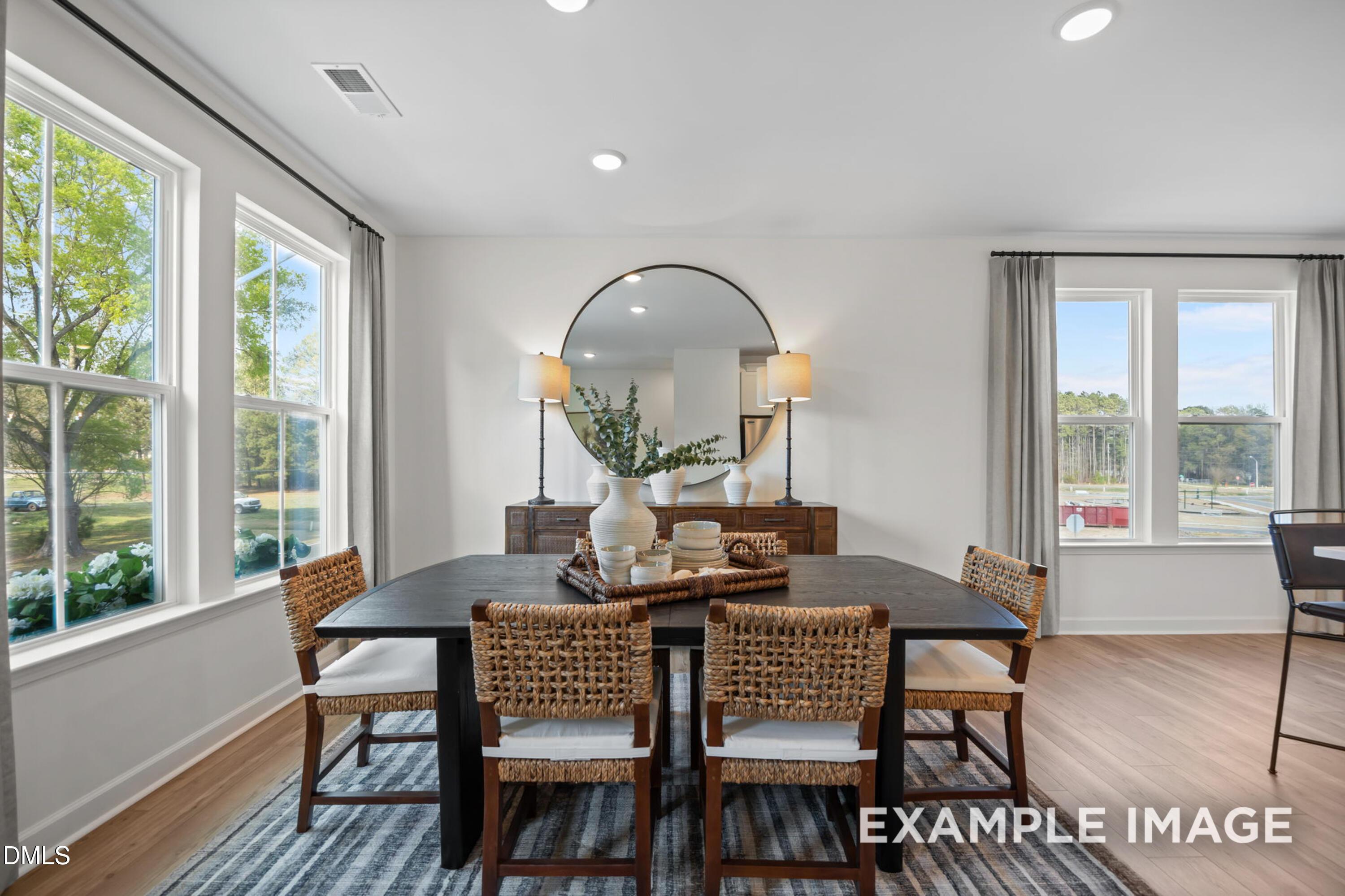 Elegant dining room with rattan chairs, dark wood table, large windows, round mirror in Davidson Homes The Mitchell, Knightdale, NC